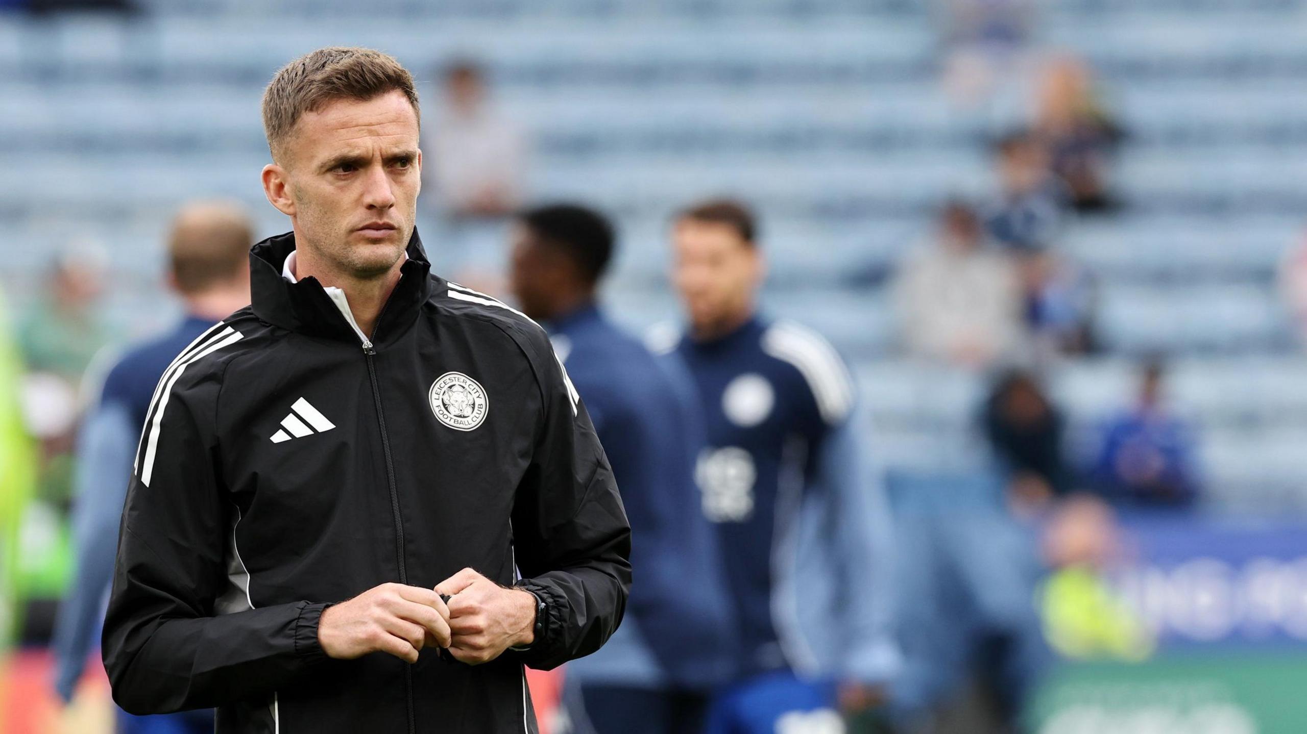 Leicester City coach Andy King with his hands together as he watches Leicester City warm up on the pitch