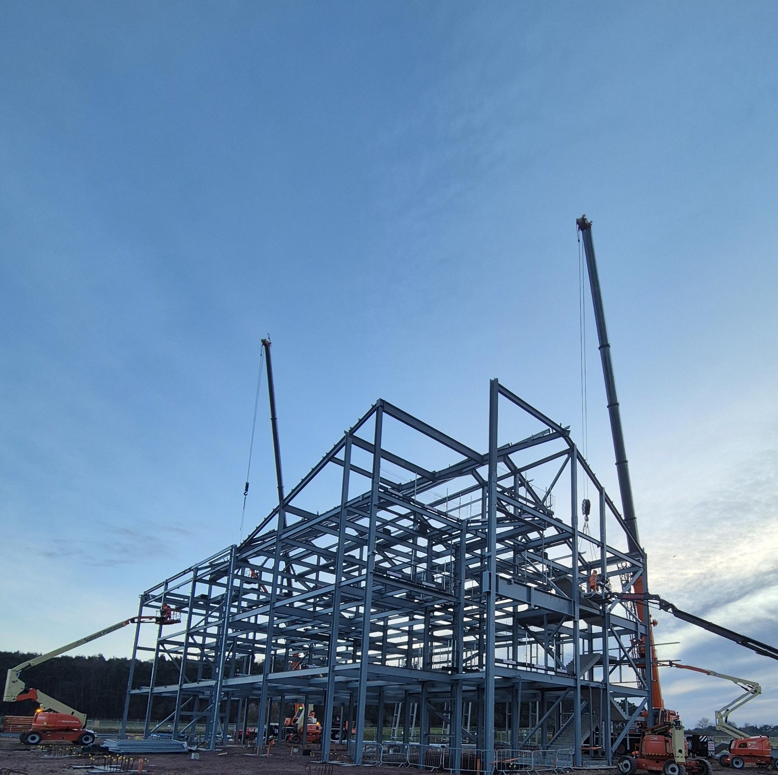 The steel frame of the new school buildings being erected. There are several cranes on the site.