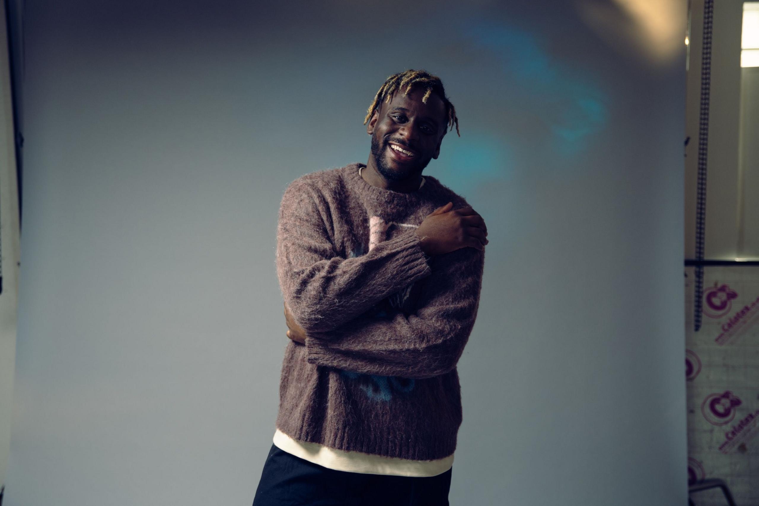 Myles Smith wraps his arms around his chest as he poses in a photographer's studio