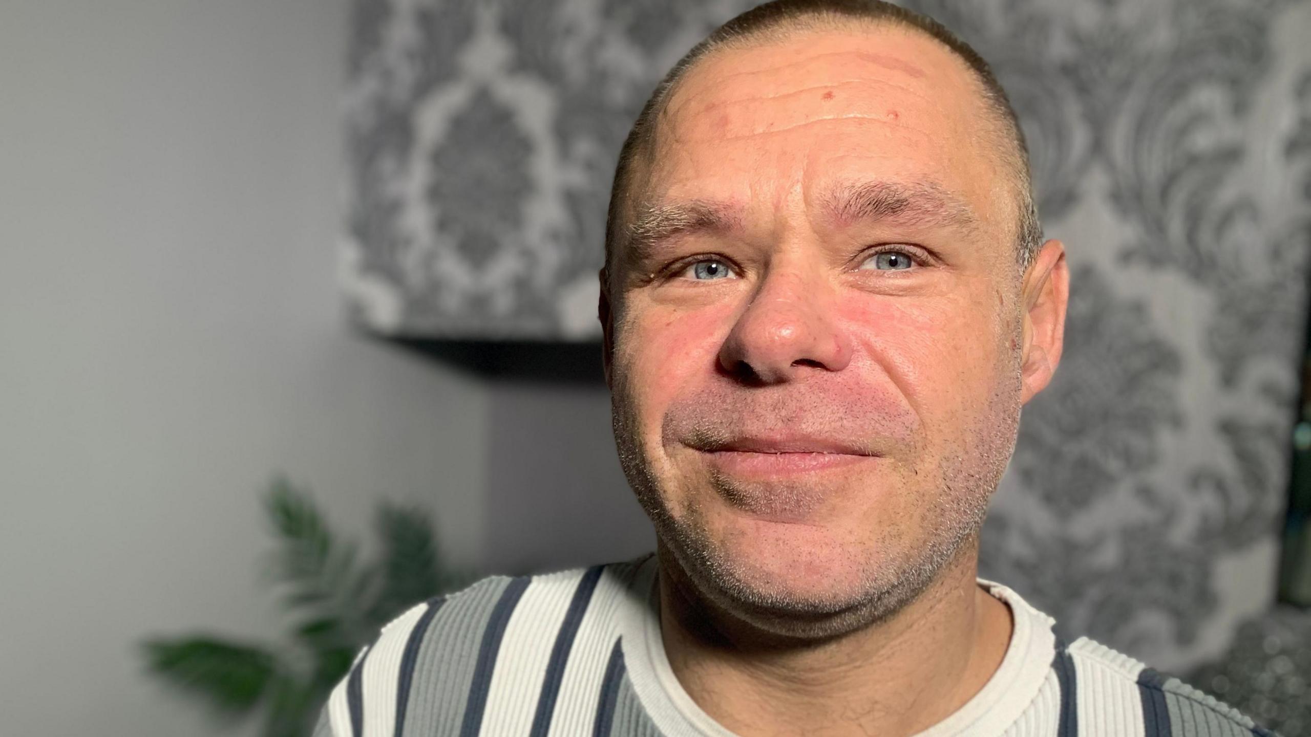 Clean shaven Stephen Ramsden has short shaved dark hair and is wearing a black, white and grey striped sweater.