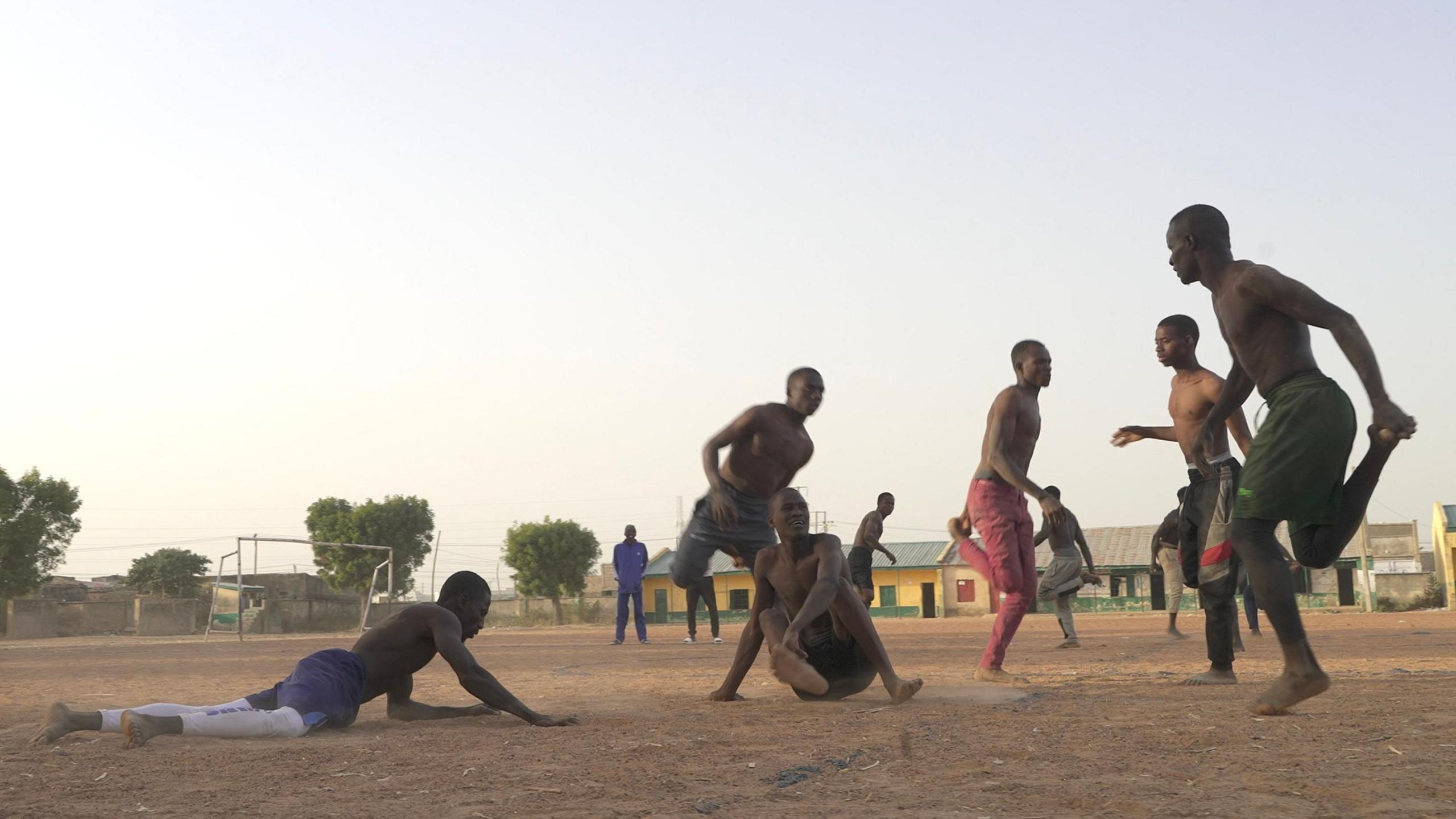 Langa players chasing each other on a sandy pitch, with two shown on the floor and seven hopping spread around in the foreground and distance