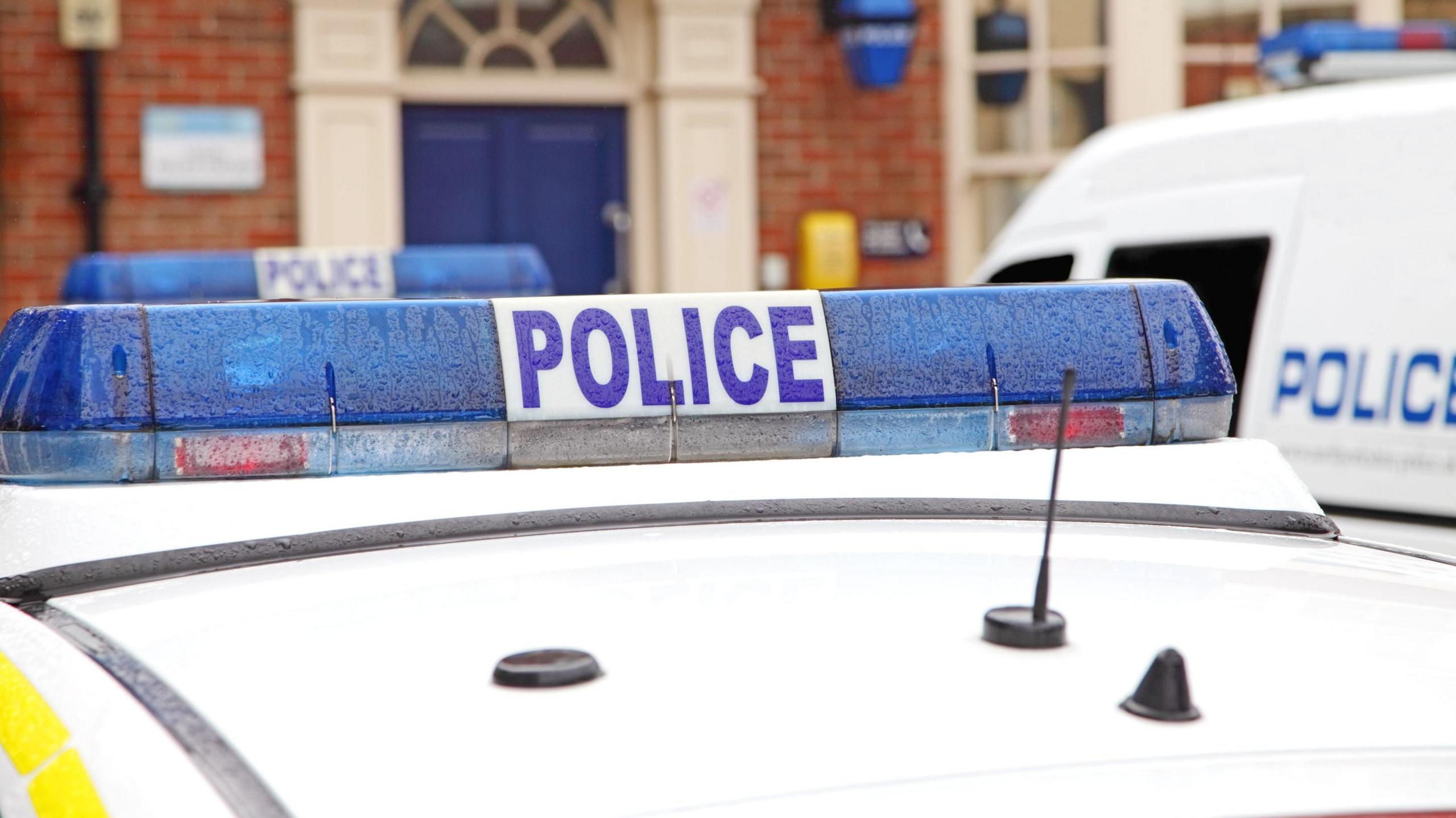 A stock image of a police officer's car. The top of the vehicle is visible with its blue lights.