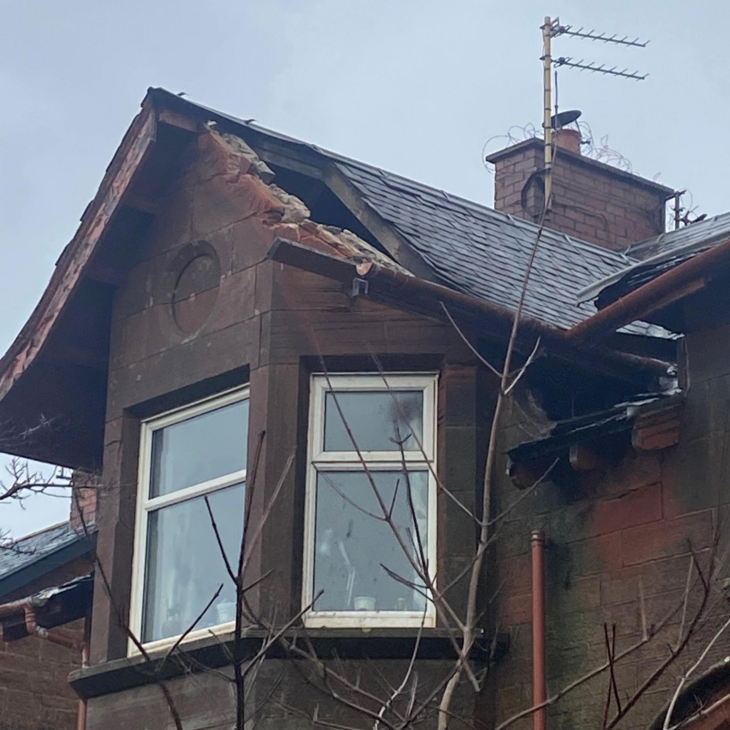 A window on the top of a Victorian sandstone house in Troon. The roof above the window has been torn off and the inside is exposed to the wind and rain.
