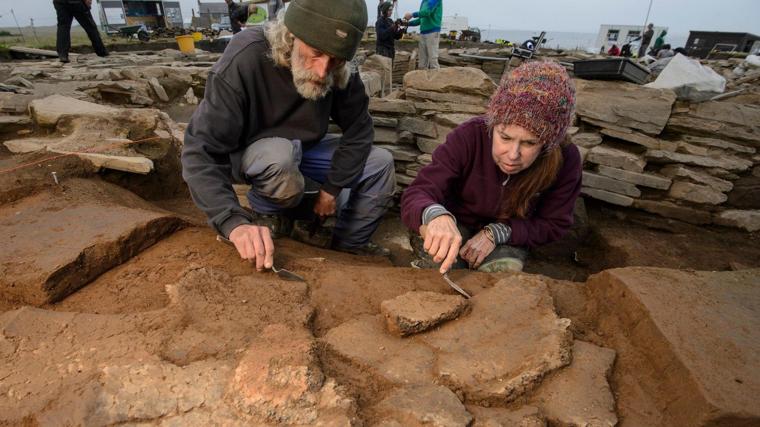 Two archaeologists working with trowels on stones at the dig 