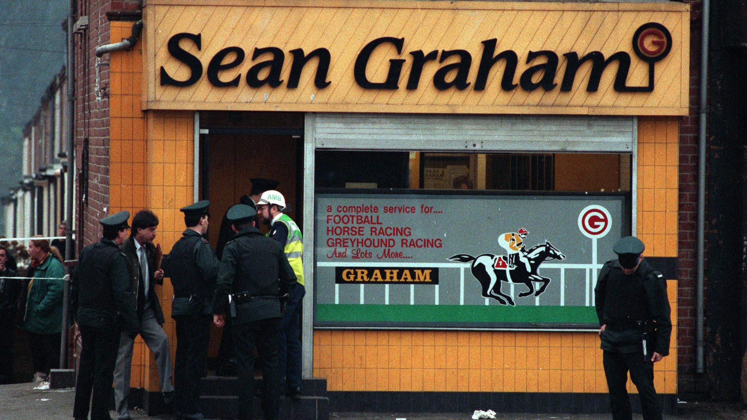 Archive image of Sean Graham bookmakers shooting. The front of the building is yellow with black writing of 'Sean Graham'. A group of police officers are outside.