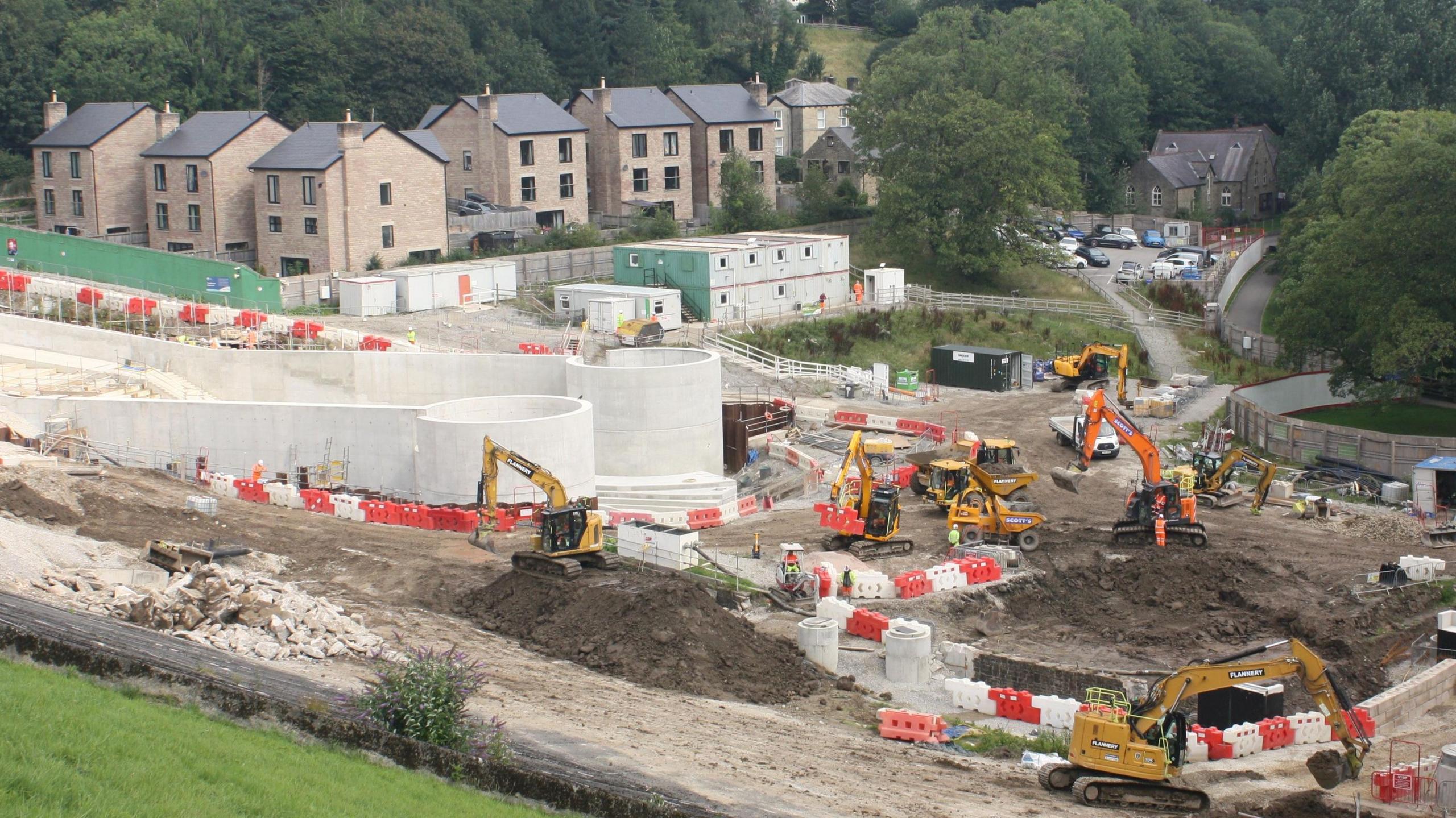 The re-designed spillway at Toddbrook Reservoir with construction vehicles on site and houses in the background