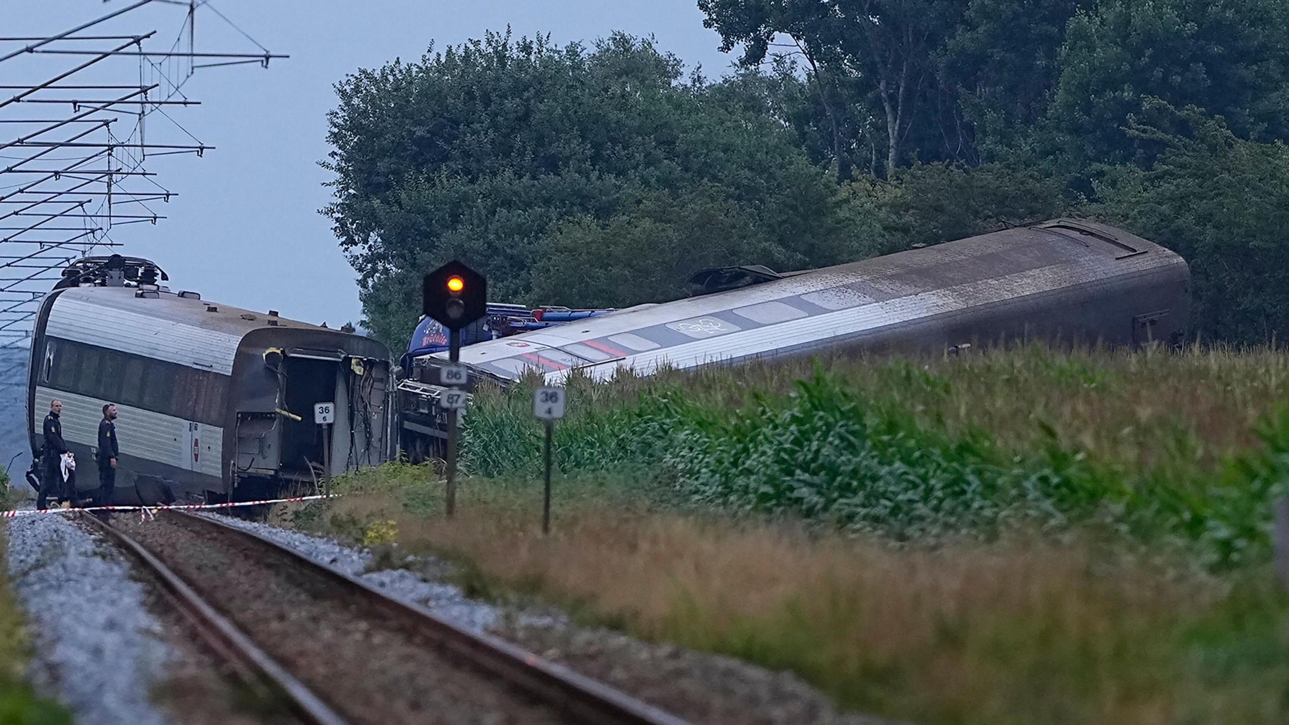 Two police look at a train carriage, which is on its side and at an angle from the engine