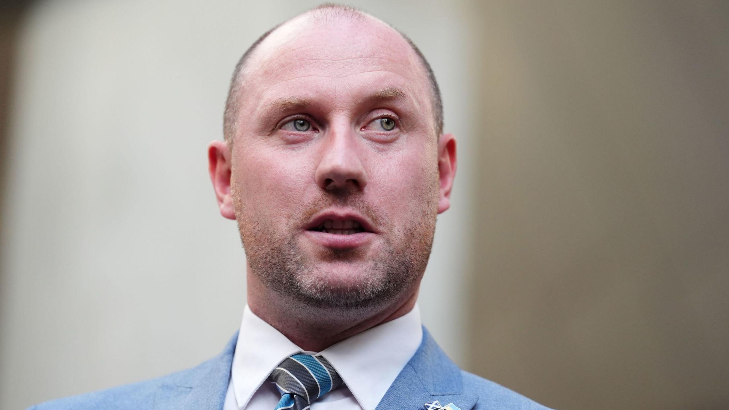 Neil Gray head and shoulders shot in blue suit and stripe tie