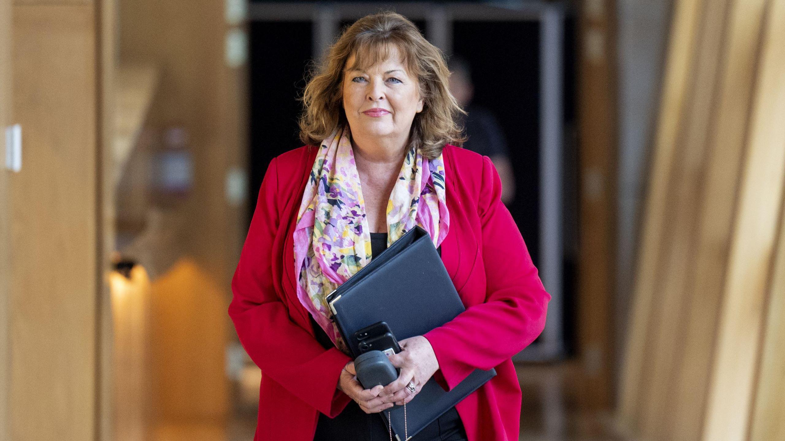 Fiona Hyslop walking through Holyrood, wearing a red jacket and a multi-coloured scarf