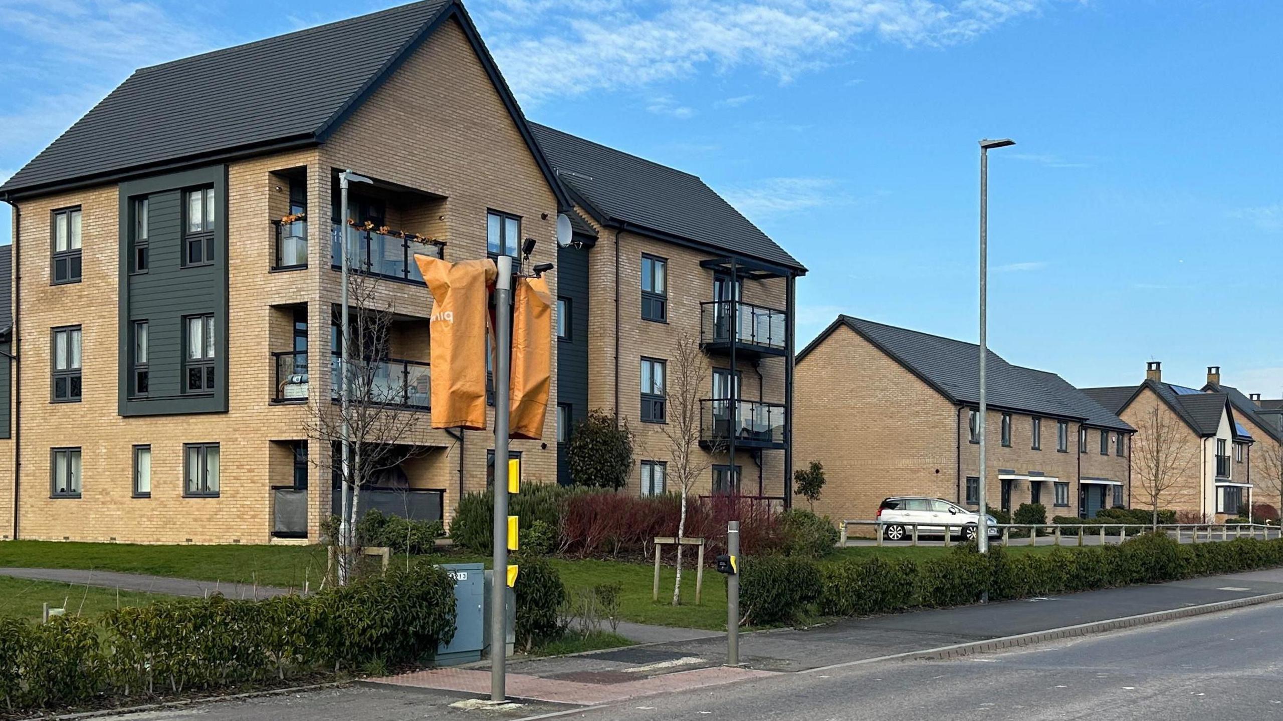 New build houses on a clear blue day. Traffic lights are covered up in orange coverings. Roads look unfinished and have faded lines.