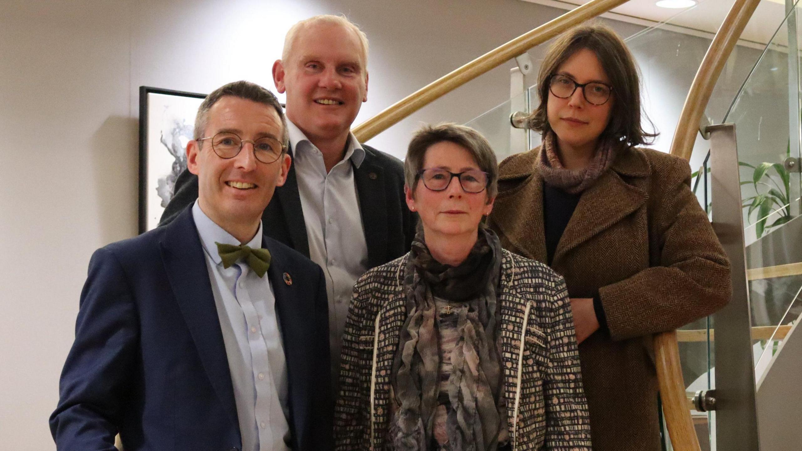 Minster Andrew Muir wearing a blue suit and bow tie, John McCallister wearing a dark suit and light, open-neck shirt, Diane Ruddock wearing glasses and a monochrome tweed coat and Viviane Gravey wearing glasses, a long, brown coat and scarf.  