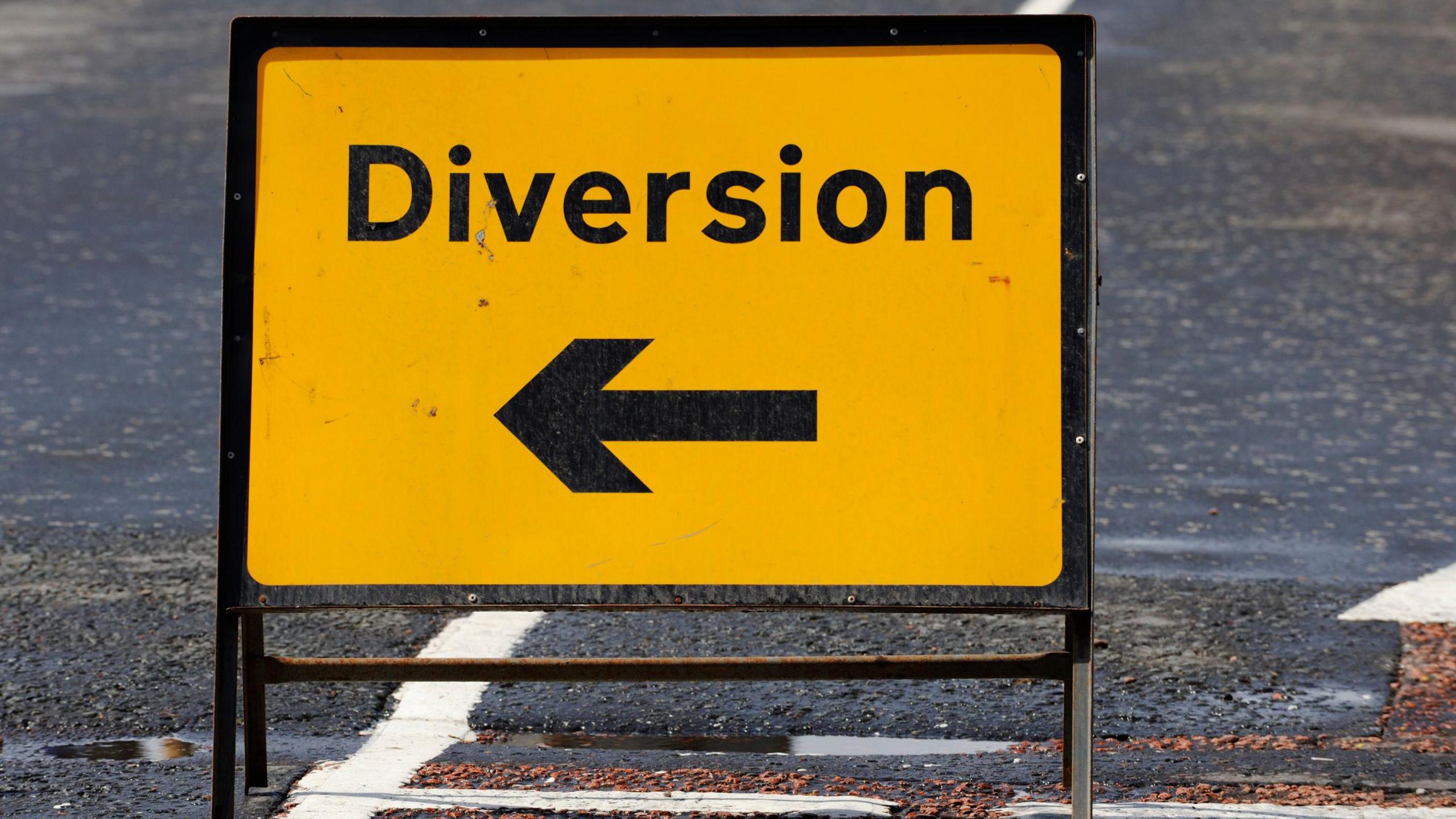 A yellow road diversion sign with a black arrow pointing drivers to the route they need to take