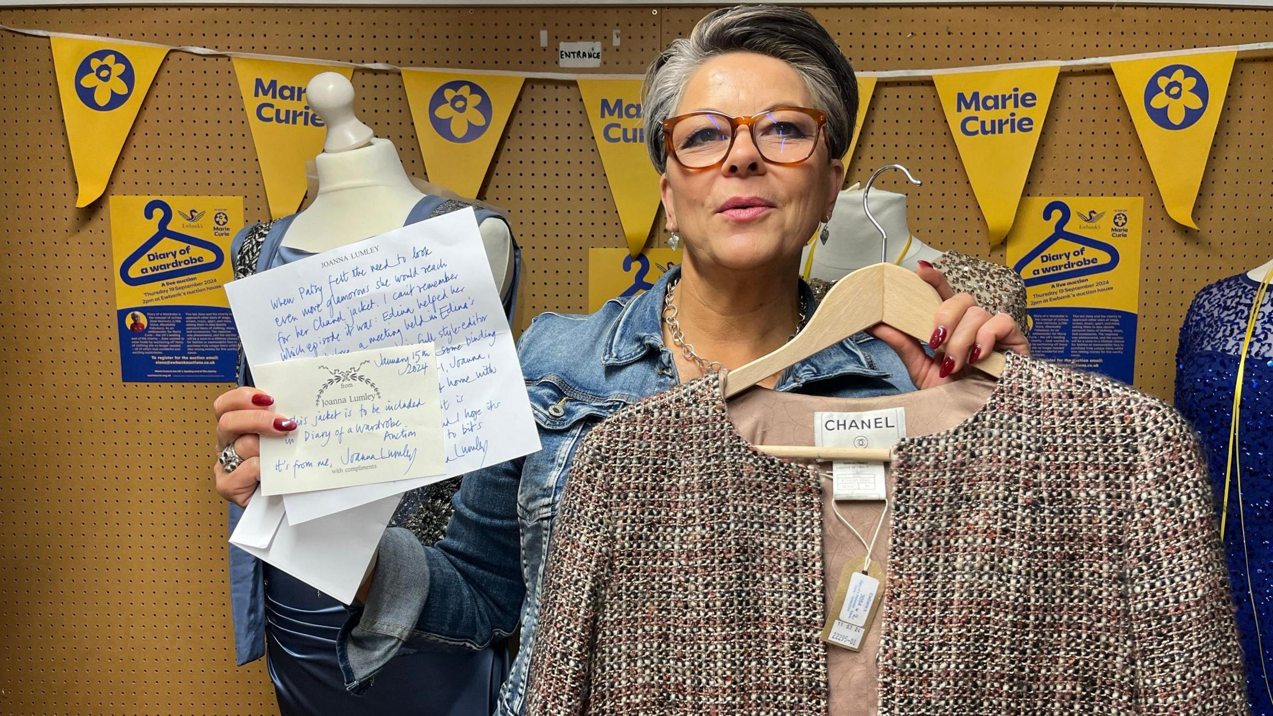 The auctioneer holds a Chanel jacket and a letter describing it from Joanna Lumley