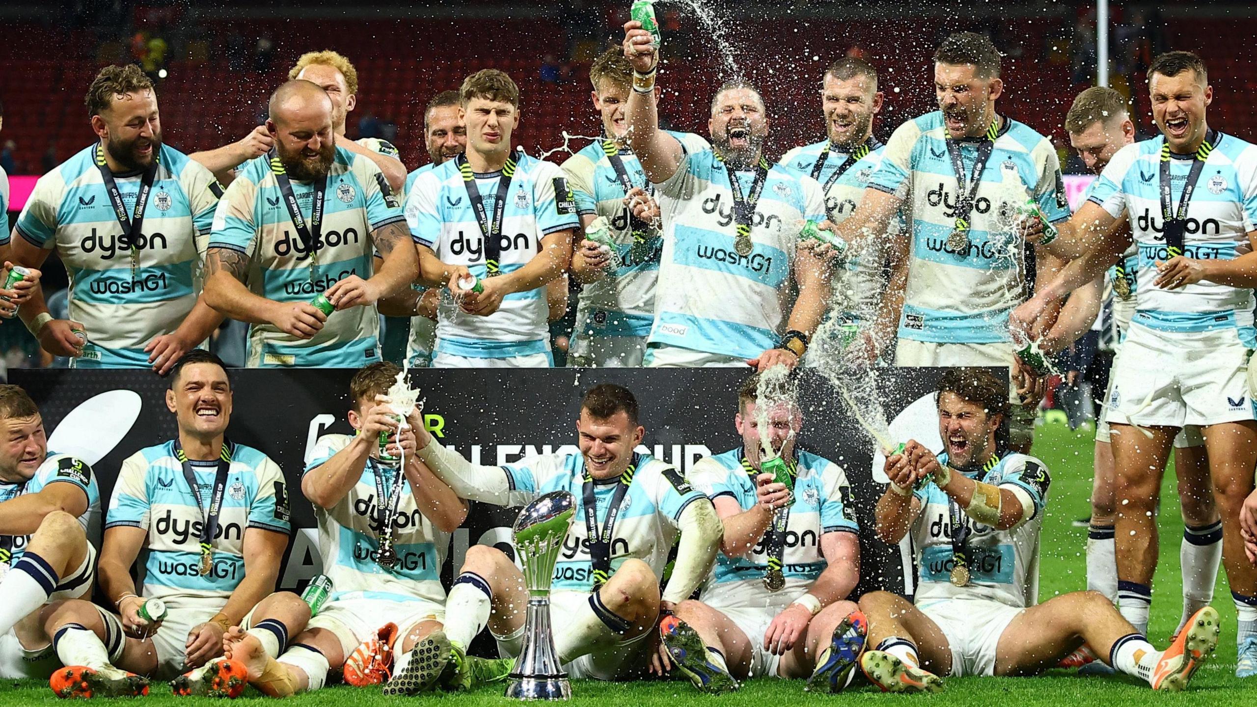 Bath players spray champagne as they stand and sit around the European Challenge Cup trophy
