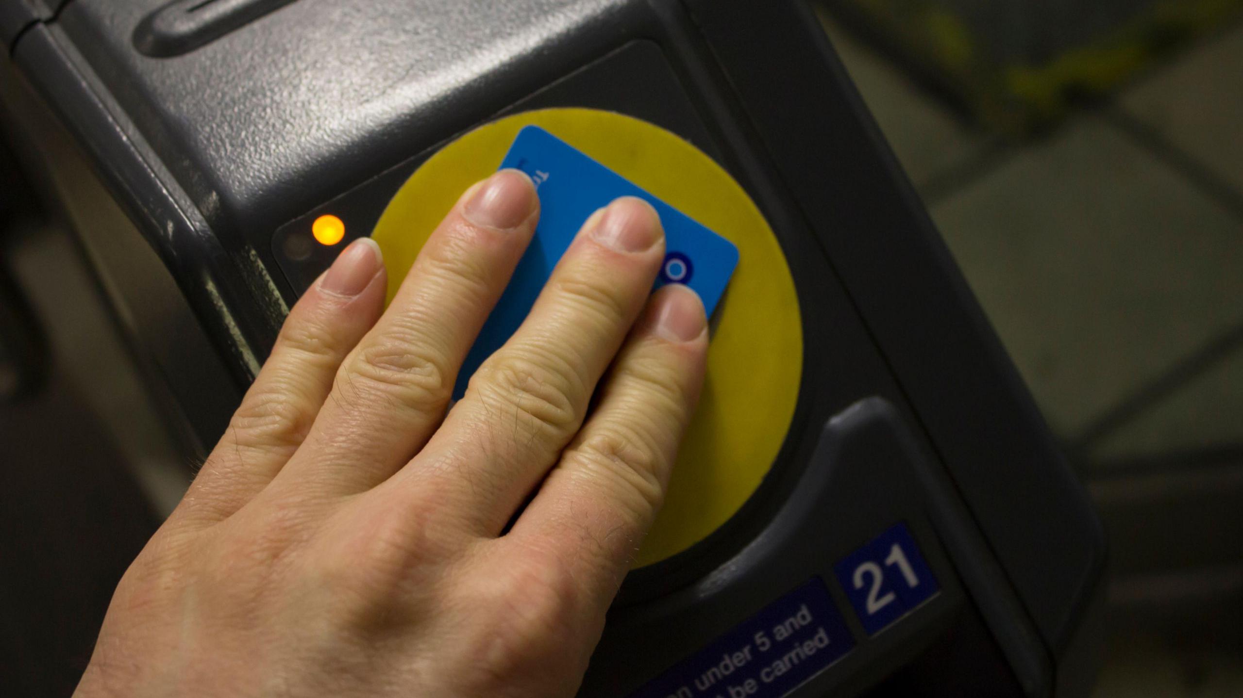 A hand places an Oyster card onto a ticket machine in London at a station