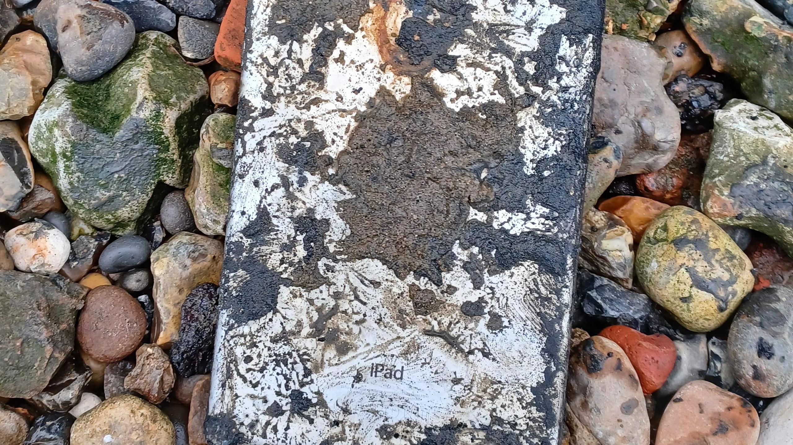 An ipad mini is caked in mud and appears damaged beyond repair. it is surrounded by rocks after it had been dug up from the river thames in november 2024.