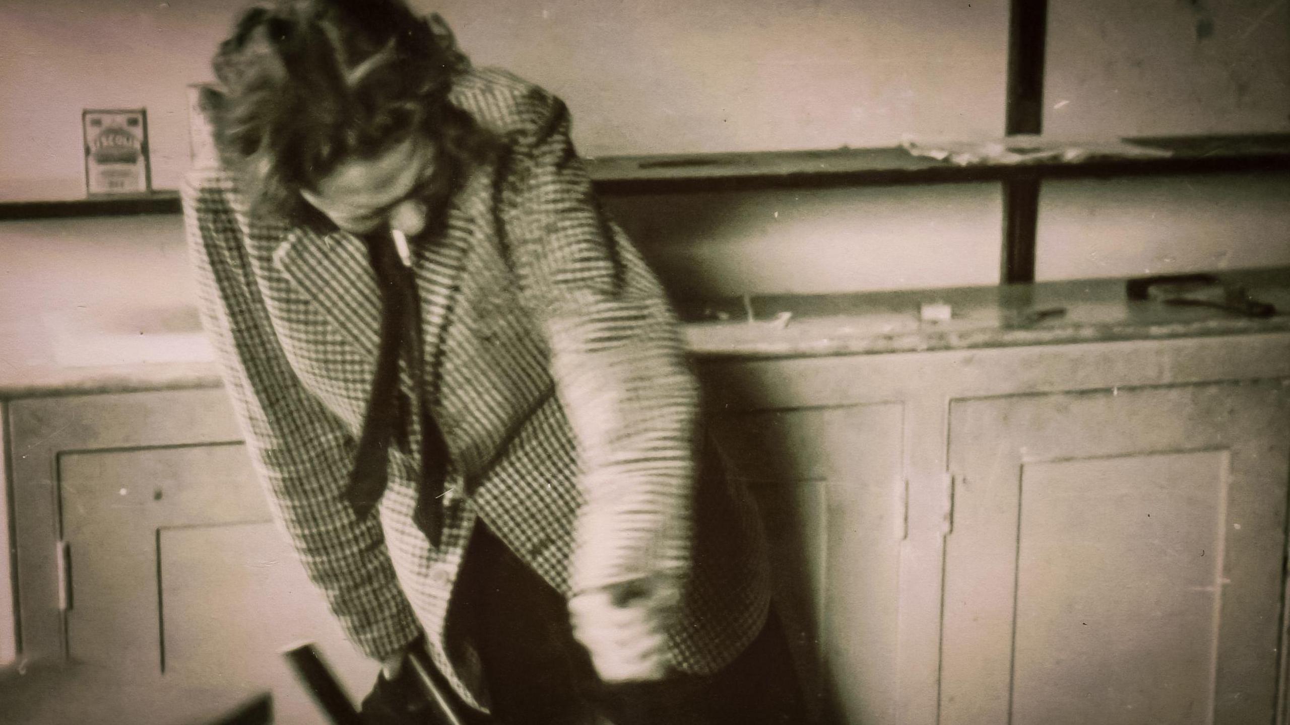 Dylan Thomas in a black and white photo his head down and cigarette in the of this mouth. He is hunched over a bit and still still twisting something unseen with his arms.