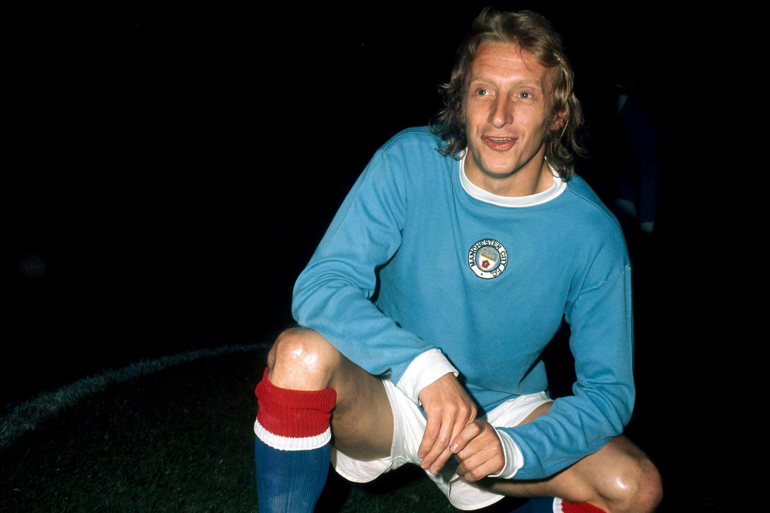 Denis Law është ulur në një gju në një fushë, i veshur me një fanellë blu të çelët të Manchester City-t me mëngë të gjata dhe një distinktiv rrethor në gjoks, pantallona të shkurtra të bardha dhe çorape të kuqe me pjesën e sipërme të bardhë. Sfondi është i errët, duke sugjeruar që fotografia është bërë gjatë natës ose nën ndriçimin e stadiumit. Duart e Law janë mbështetur në gjurin e përkulur dhe vendosja e përgjithshme tregon një foto të pozuar para ose pas një ndeshjeje.