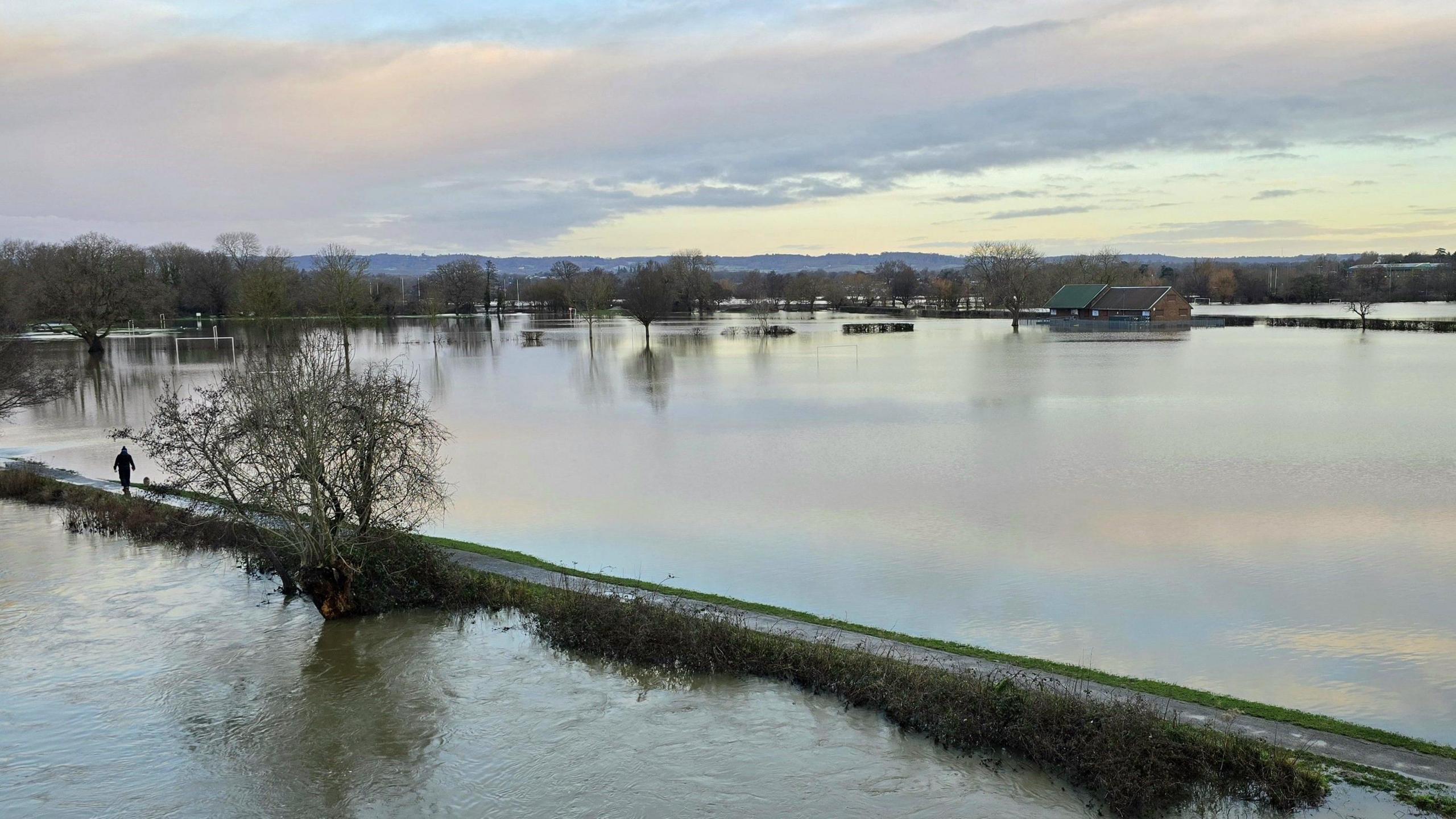 Two fields are completely flooded with a lone person walking down a raised path.