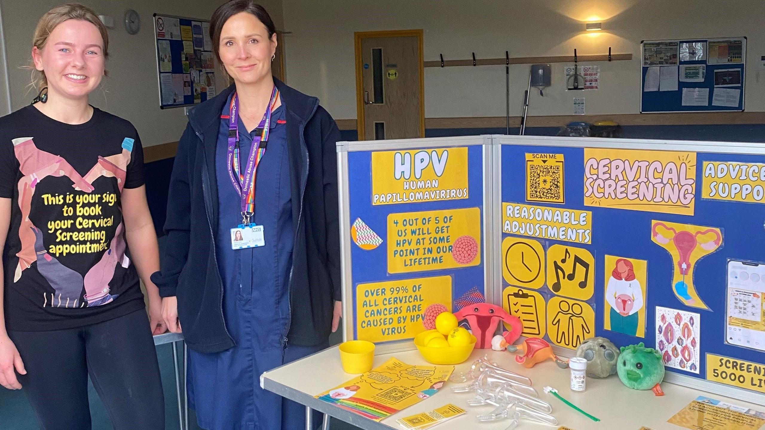 Mrs Lawrence is pictured standing next to another woman in a nurse uniform. The second woman has dark hair which is tied back and she has an ID card around her neck. They are standing next to the cervical screening stand at the Kesgrave Parkrun.