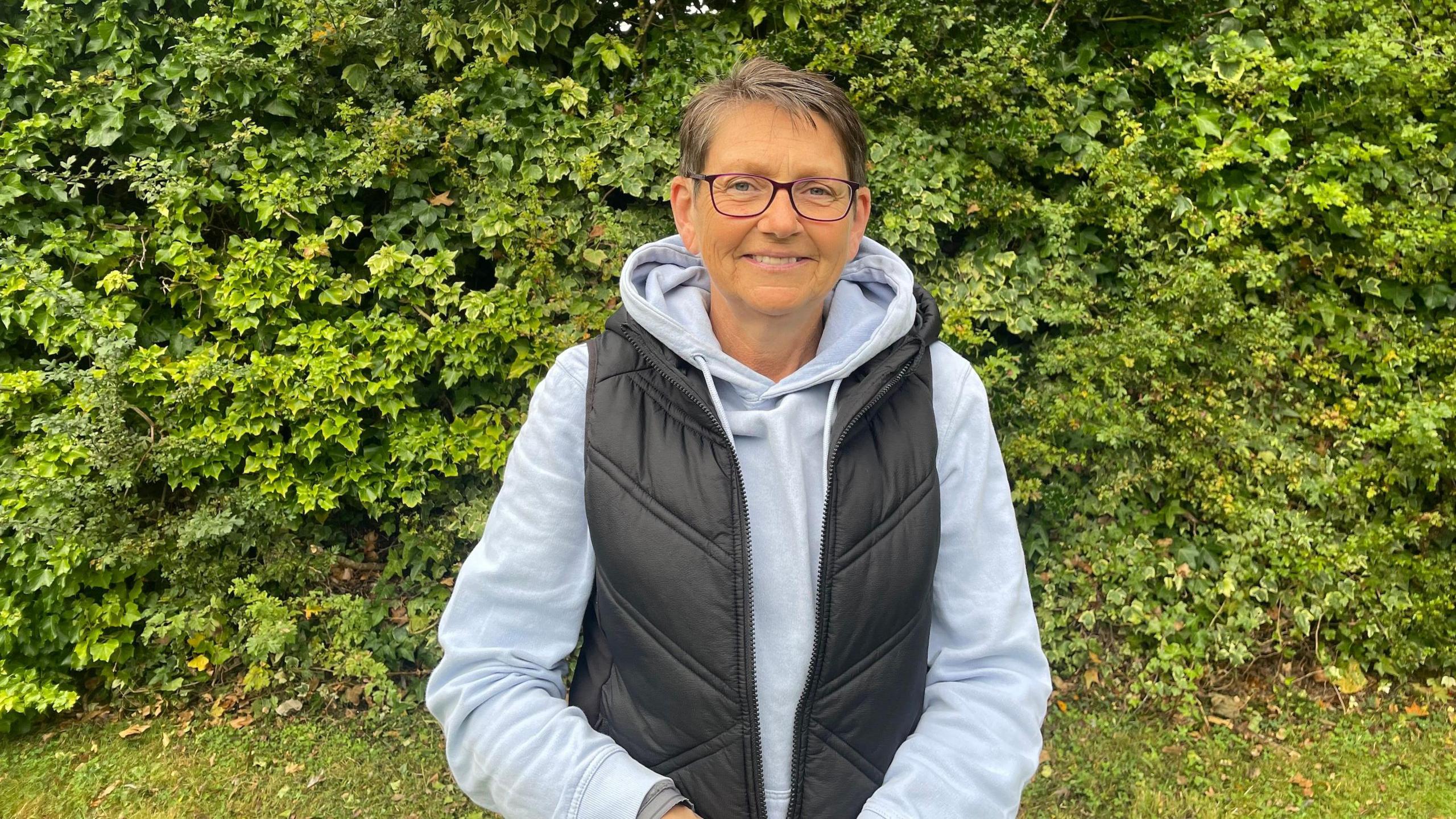 Holmes Chapel Pride committee member Alison Wright, wearing a grey hoodie and black gilet, smiles as she poses for the camera.