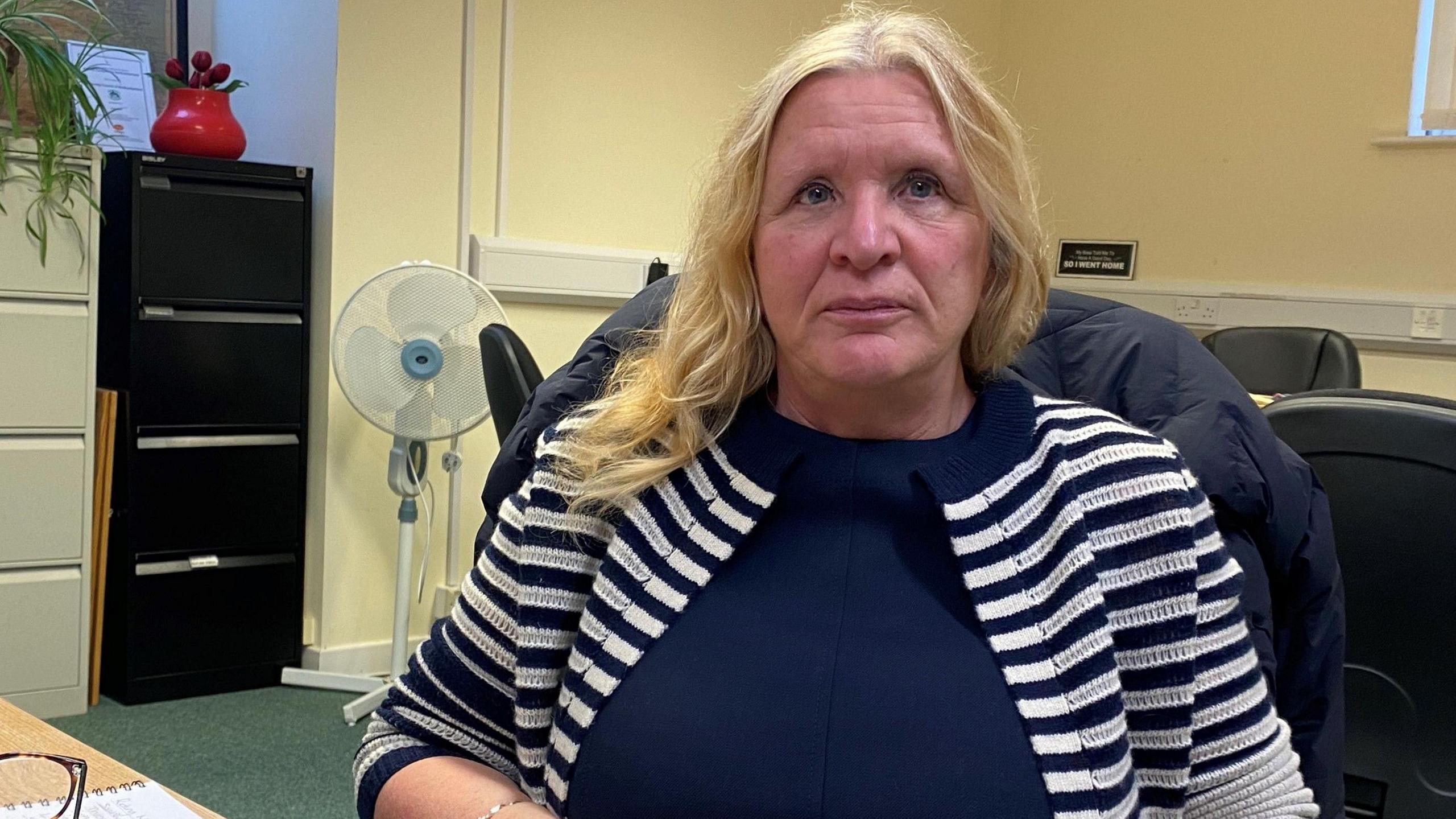 Christine Nicholls, wearing a blue and white top in front of a laptop looking straight at the camera.