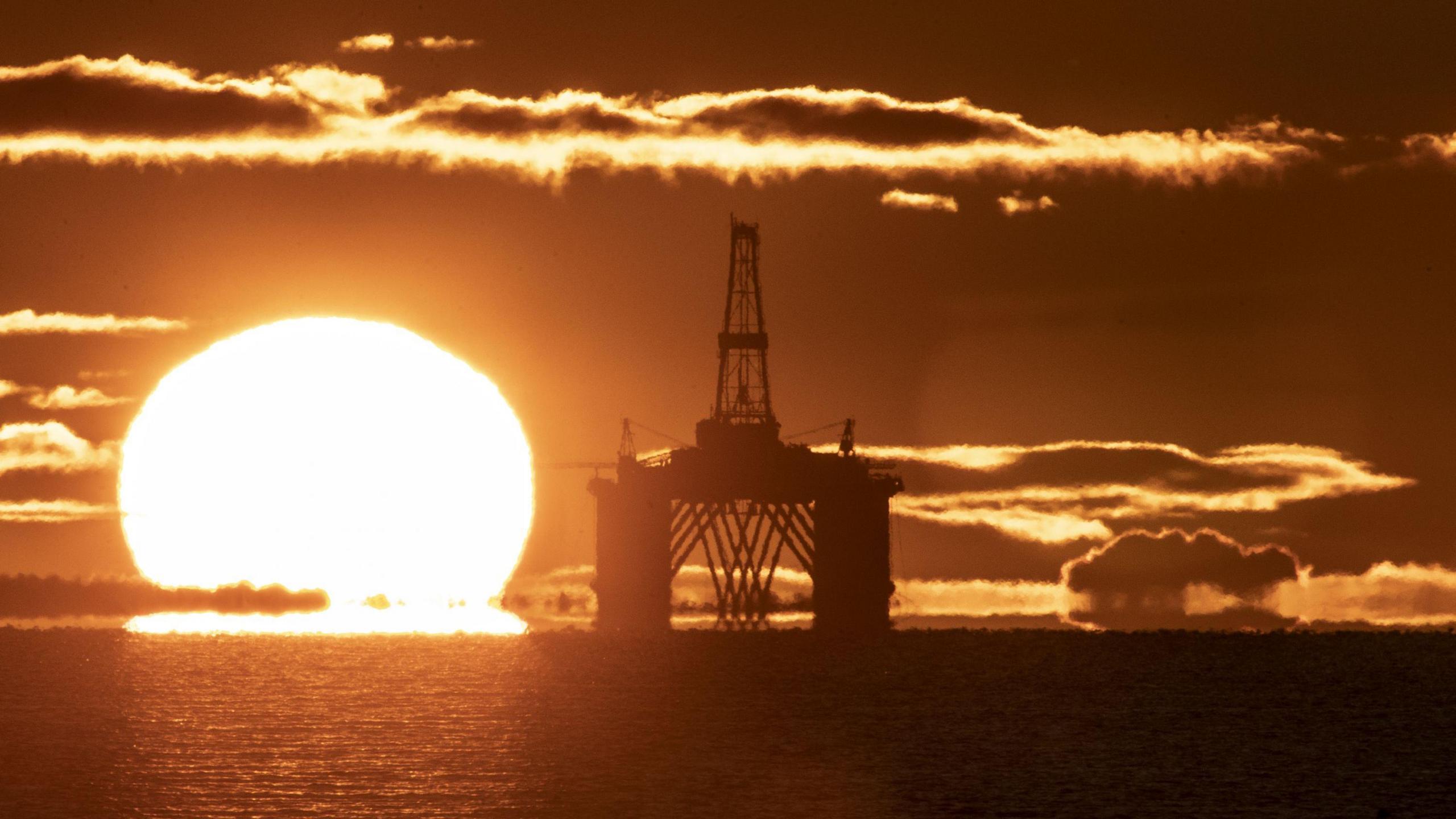 The sun behind an oil rig in the North Sea. The photo is an orange colour because of the light.
