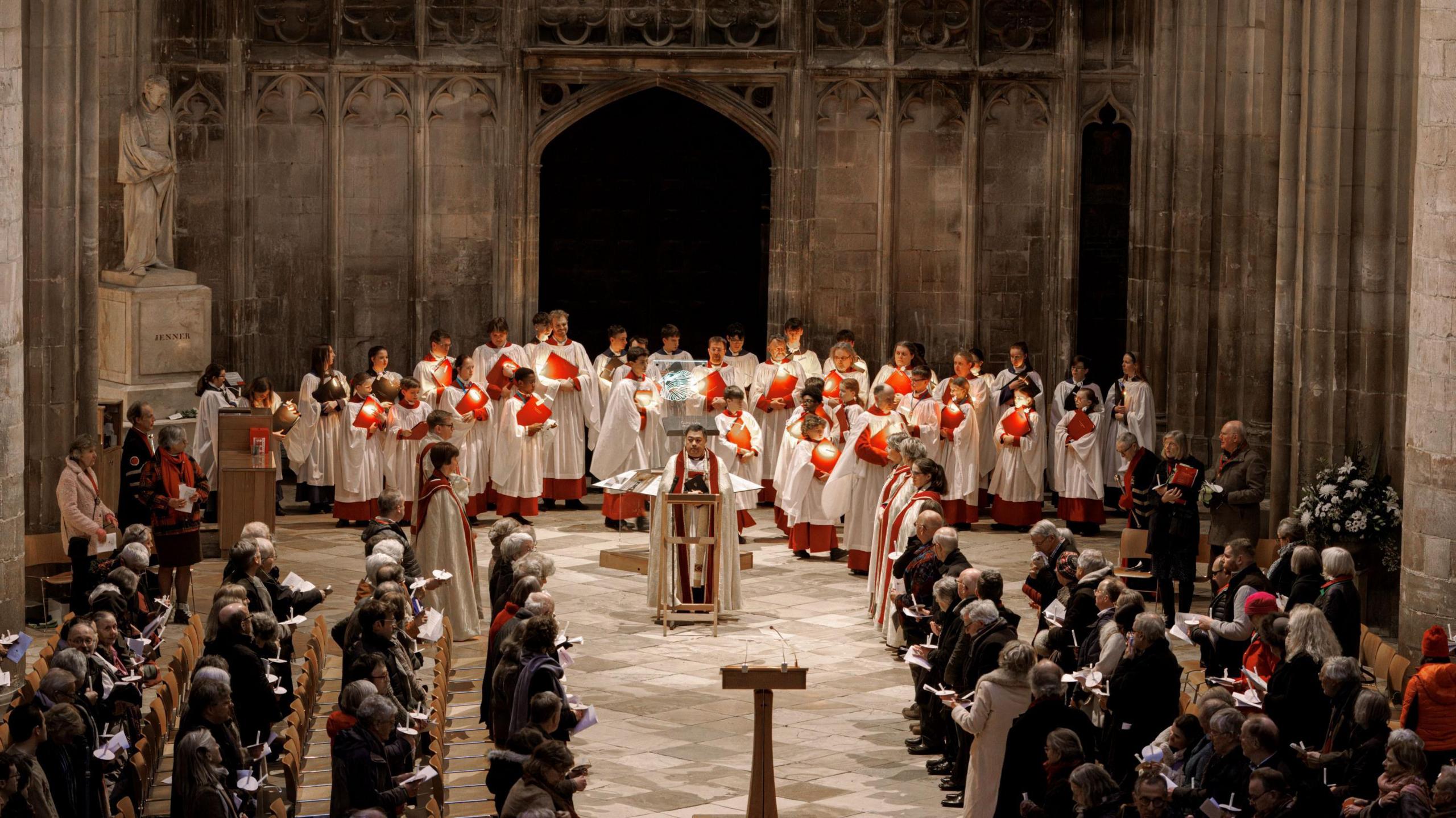 Parishioners and choir members are seen standing and singing inside Gloucester Cathedral as part of the Candlemas service. The image is taken from a slightly raised position