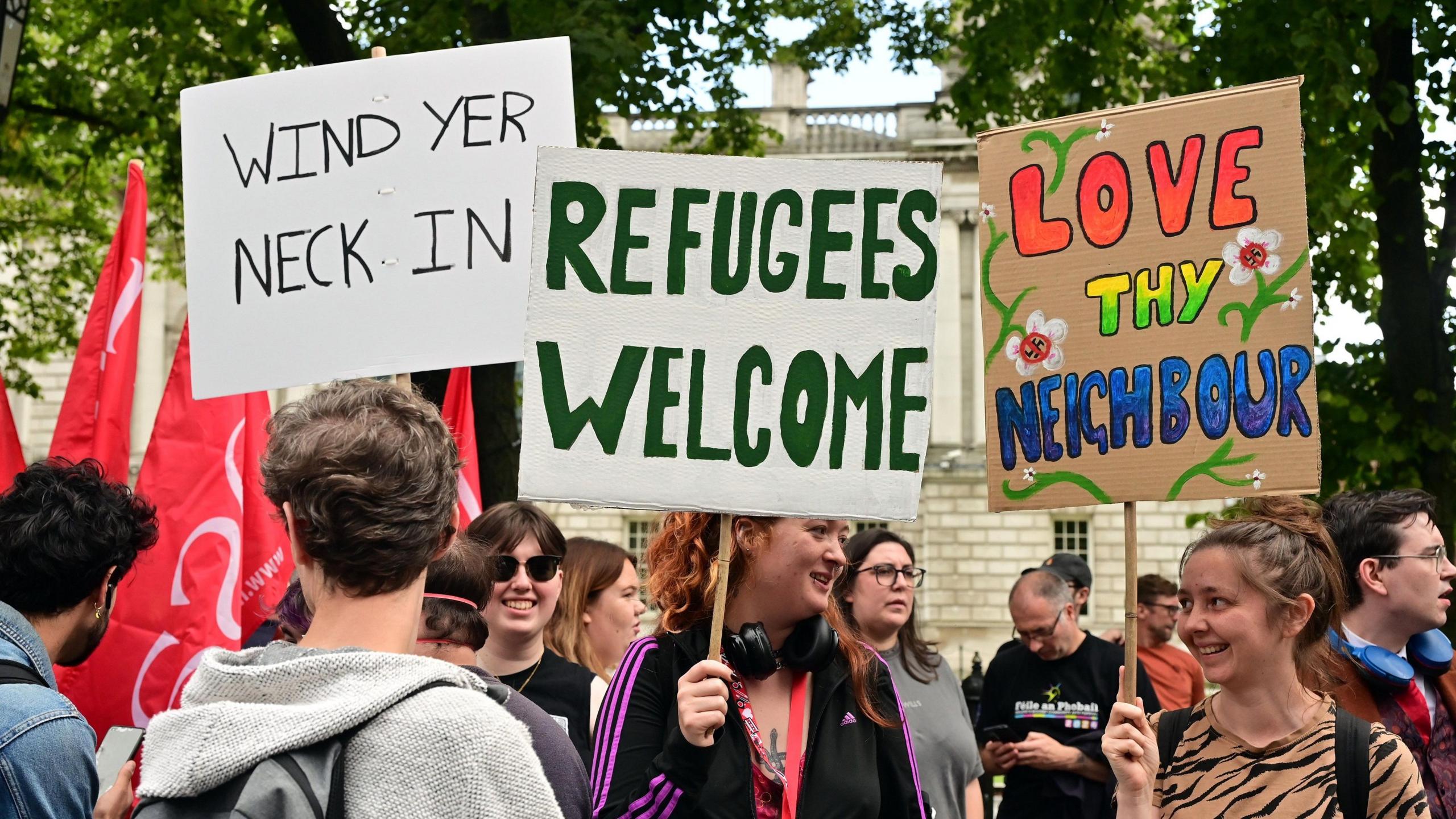 Placards at an anti racism rally in Belfast saying Refugees welcome and Wind Your Neck In