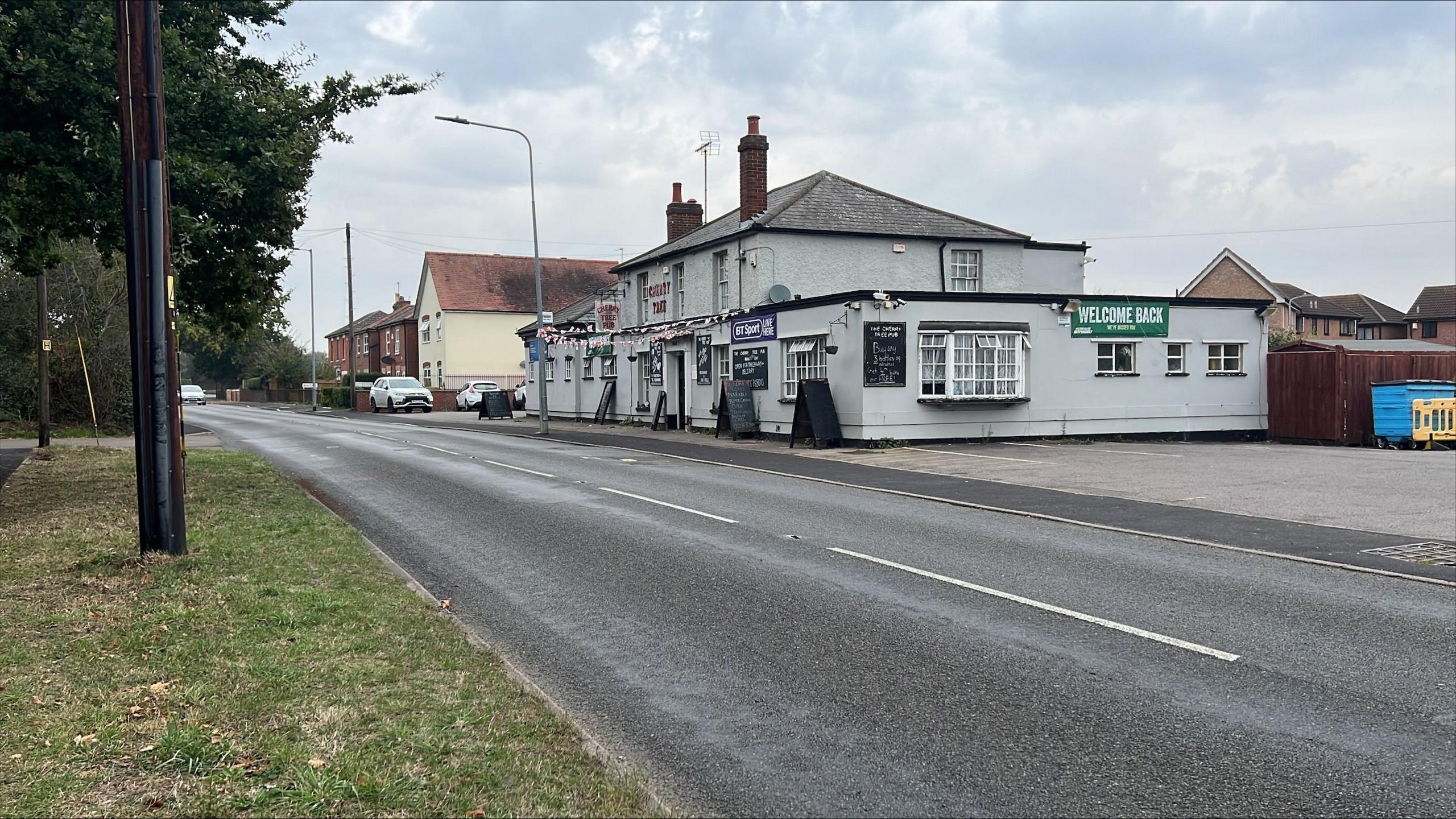 Mersea Road, Colchester. An off-white pub can be seen on the far side of the two-lane road. 