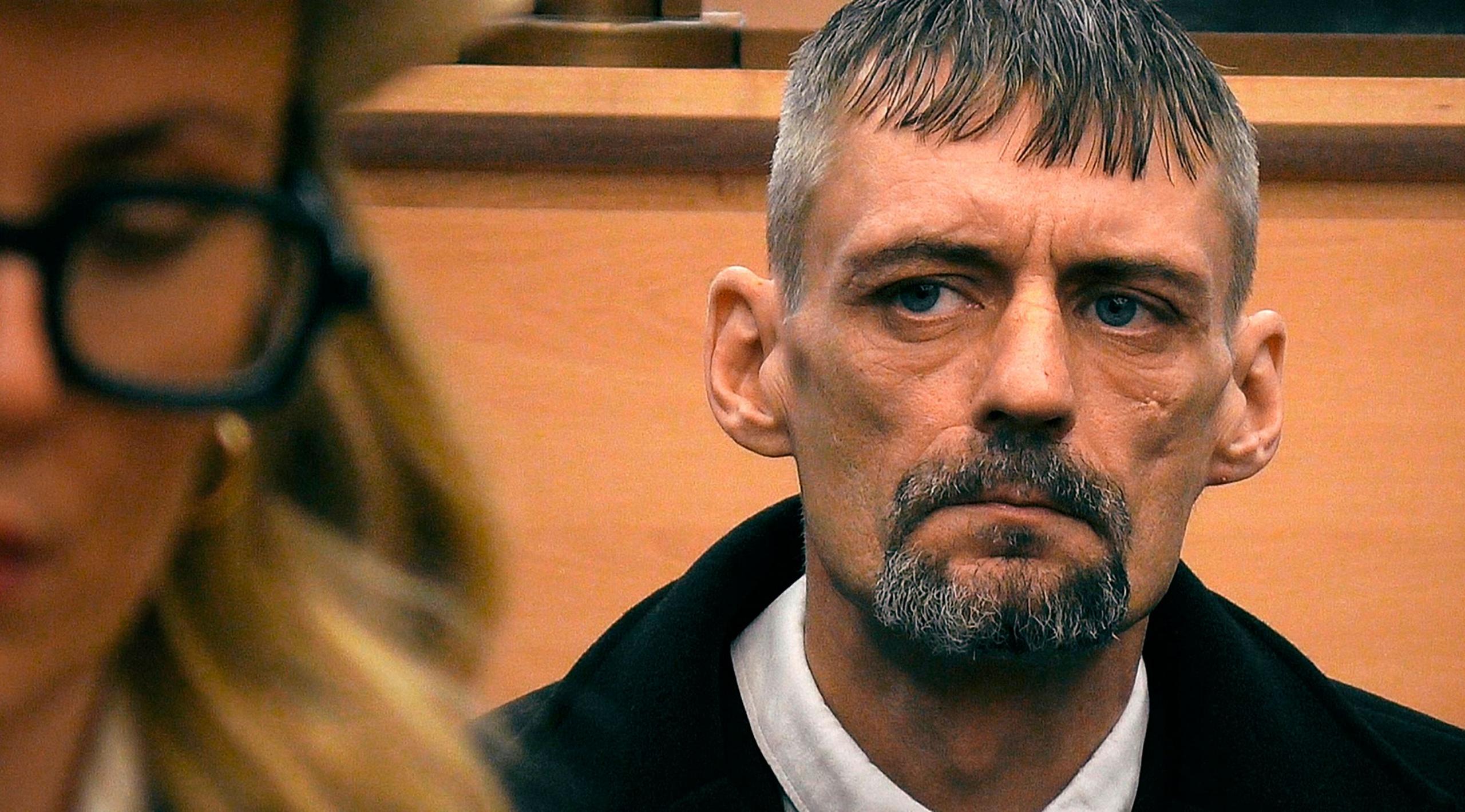 Photo of Andrew Kelly in court. He has short grey hair which is combed down at the front and greying goatee beard. He is wearing a black jacket and white shirt. 