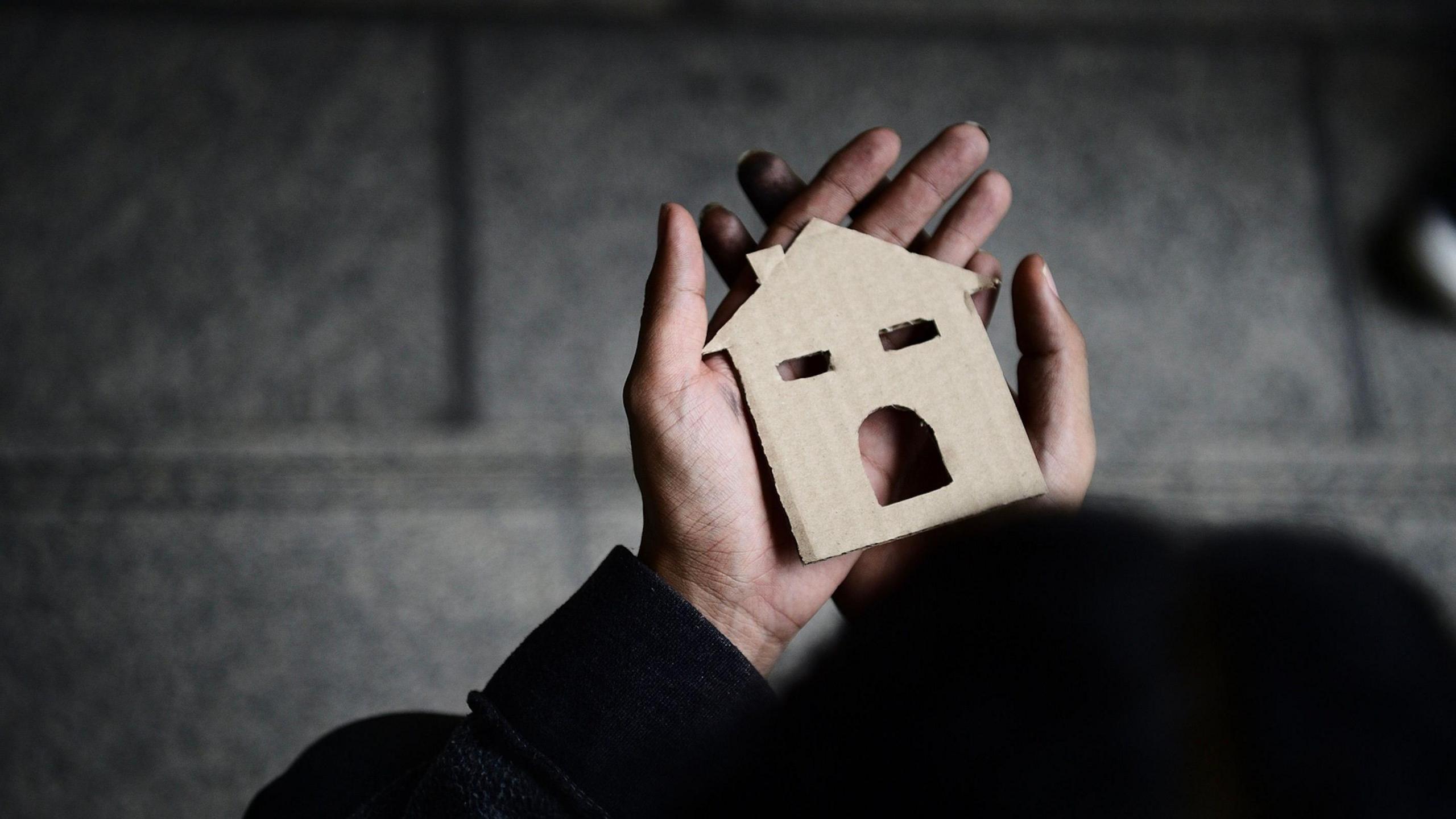 Hands holding a paper cutout of a house.