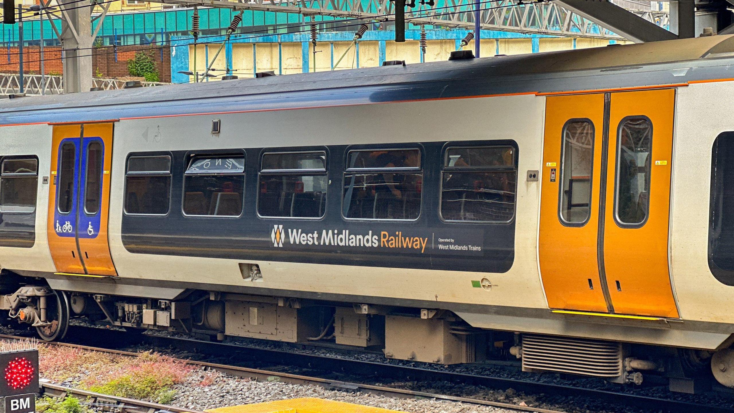 A West Midlands Railway train at a train station. It has the company name on the side, with yellow double doors.