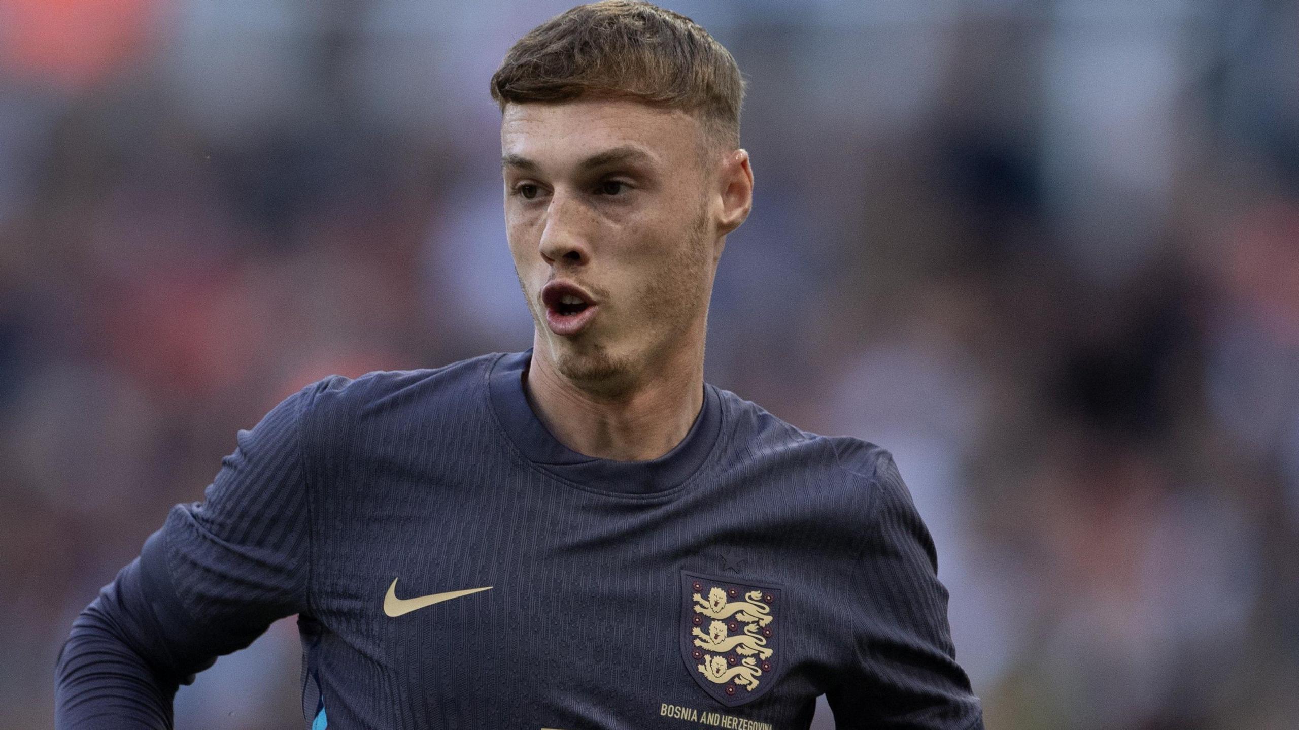 A close up of Cole Palmer, wearing the dark blue England away strip, looks over to his right