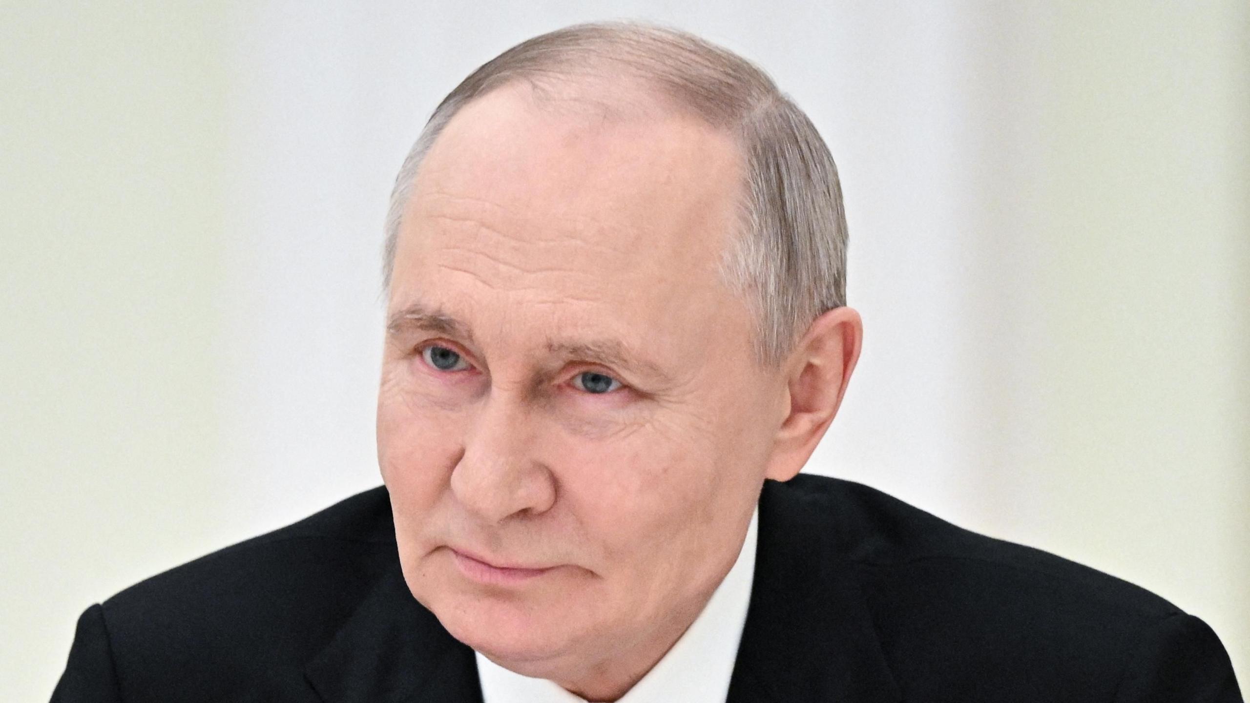 Big close-up of Vladimir Putin, wearing black jacket and white shirt