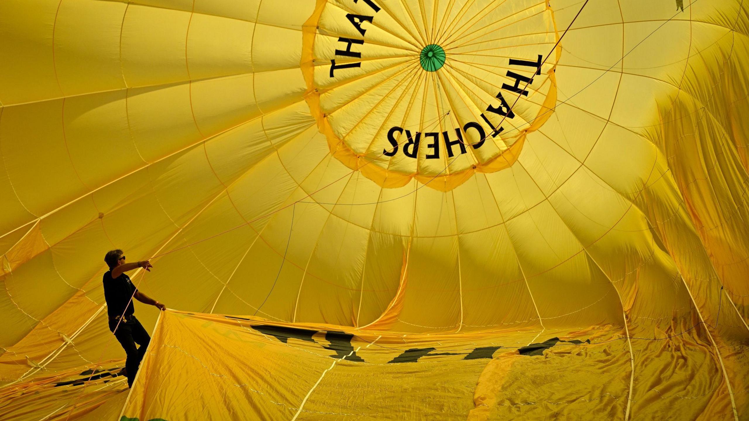 A man stands inside the canopy of a yellow Thatchers hot air balloon