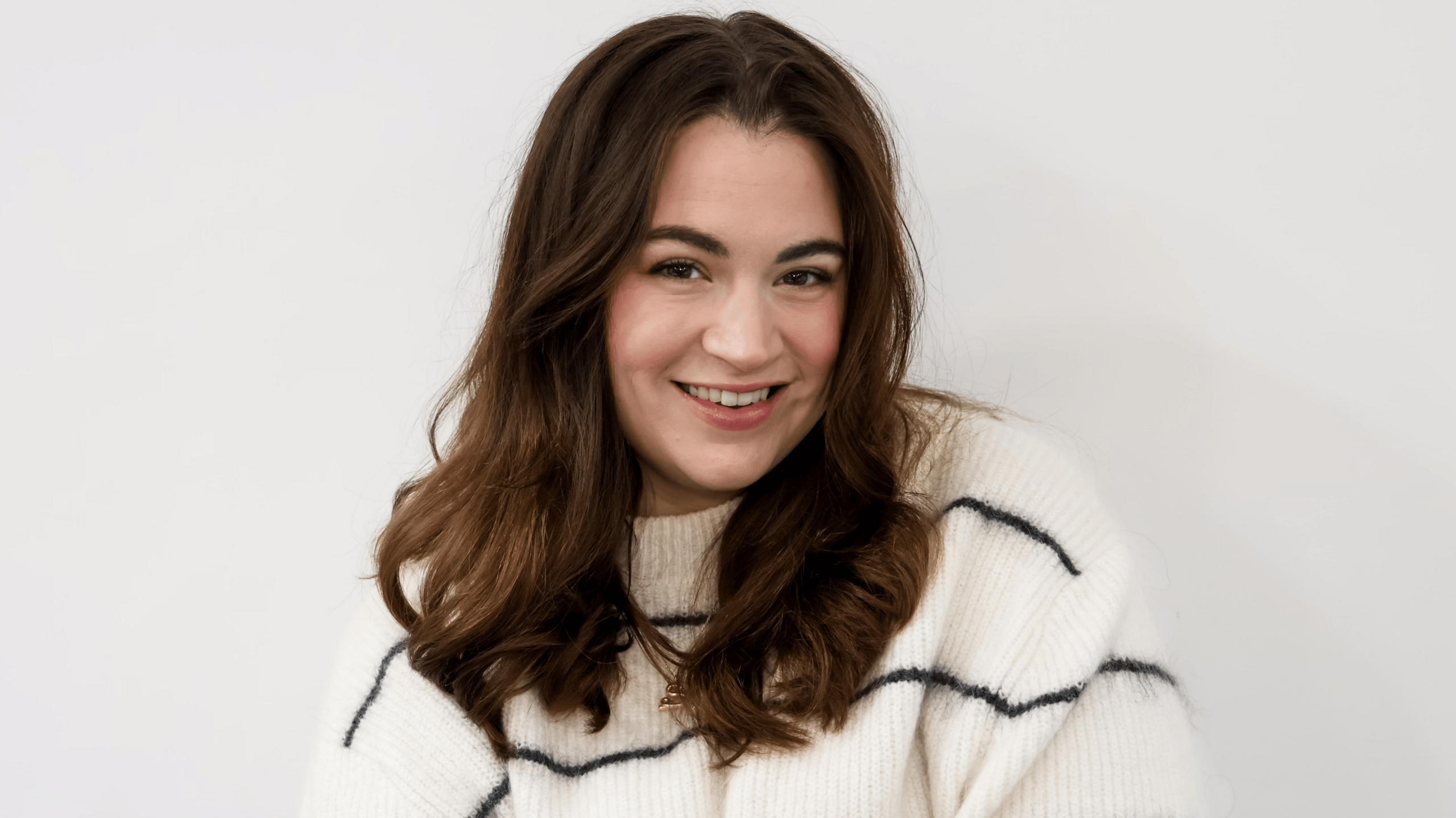 Abby Simms, from Nottingham City Council, pictured in a white jumper with thin black stripes. She has wavy brown hair and is smiling at the camera.