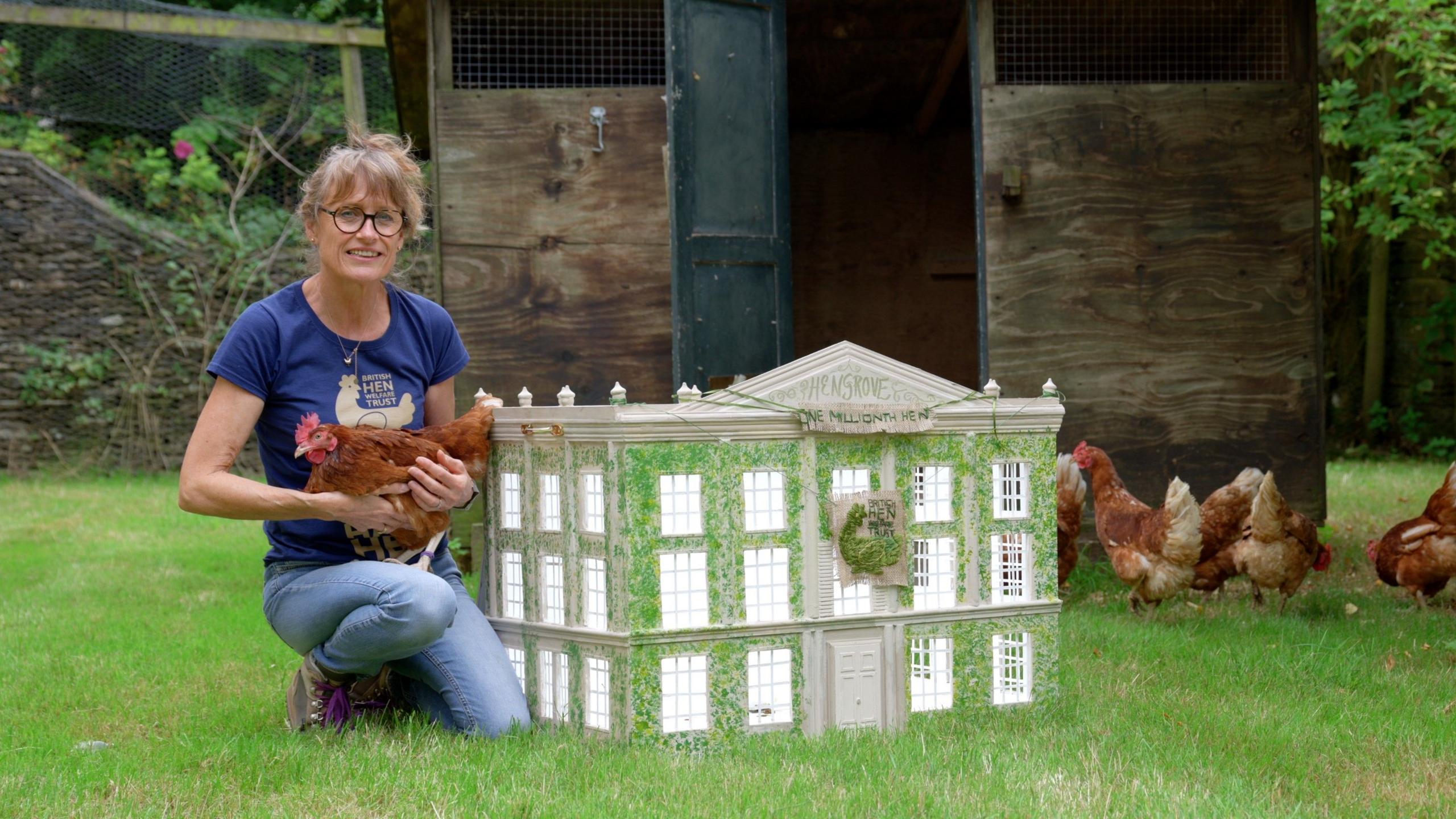 Charity CEO holding chicken next to model of Highgrove House