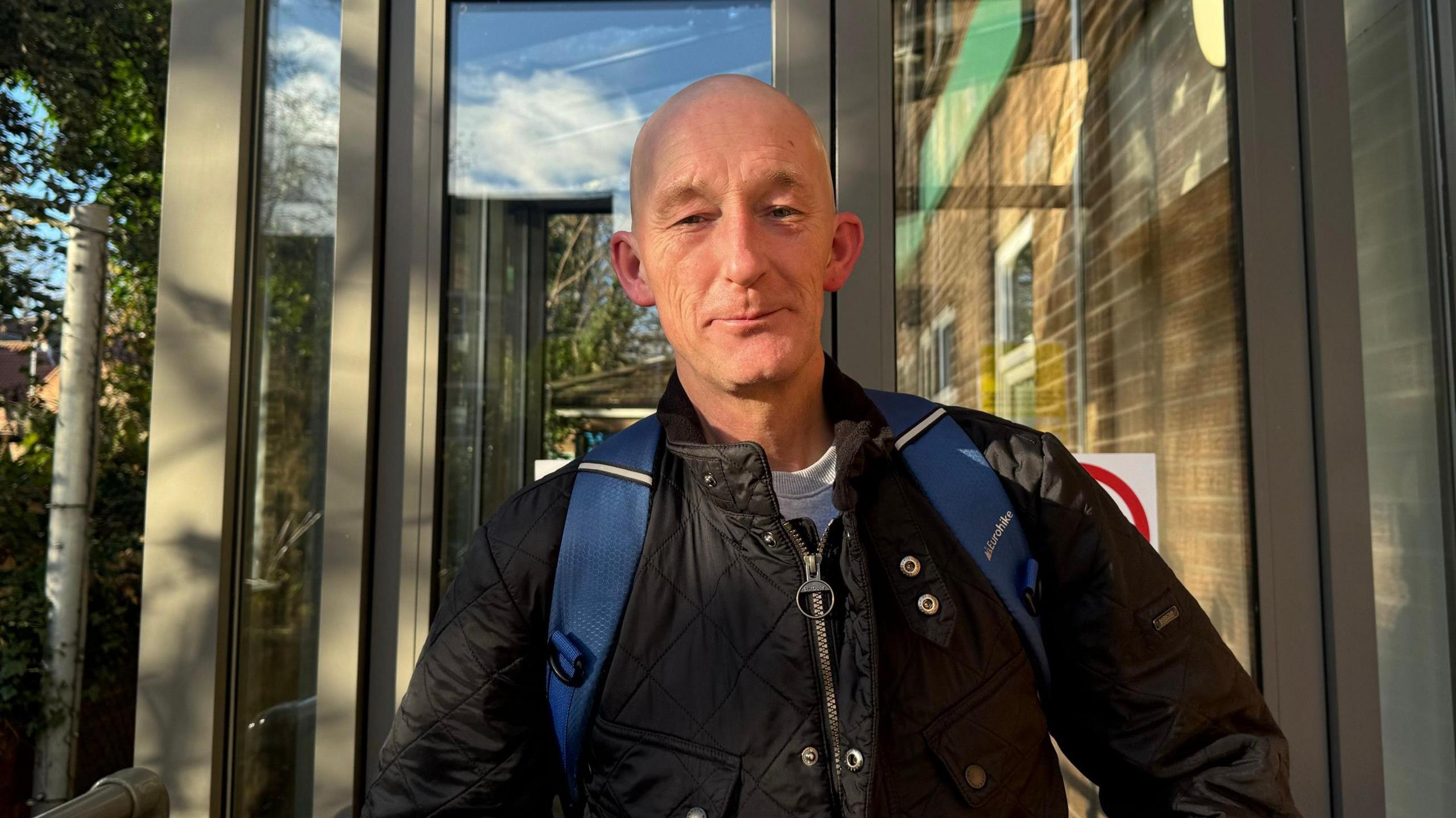 Geoffrey, who wears a black coat and blue backpack, stands outside the Jobcentre in York.