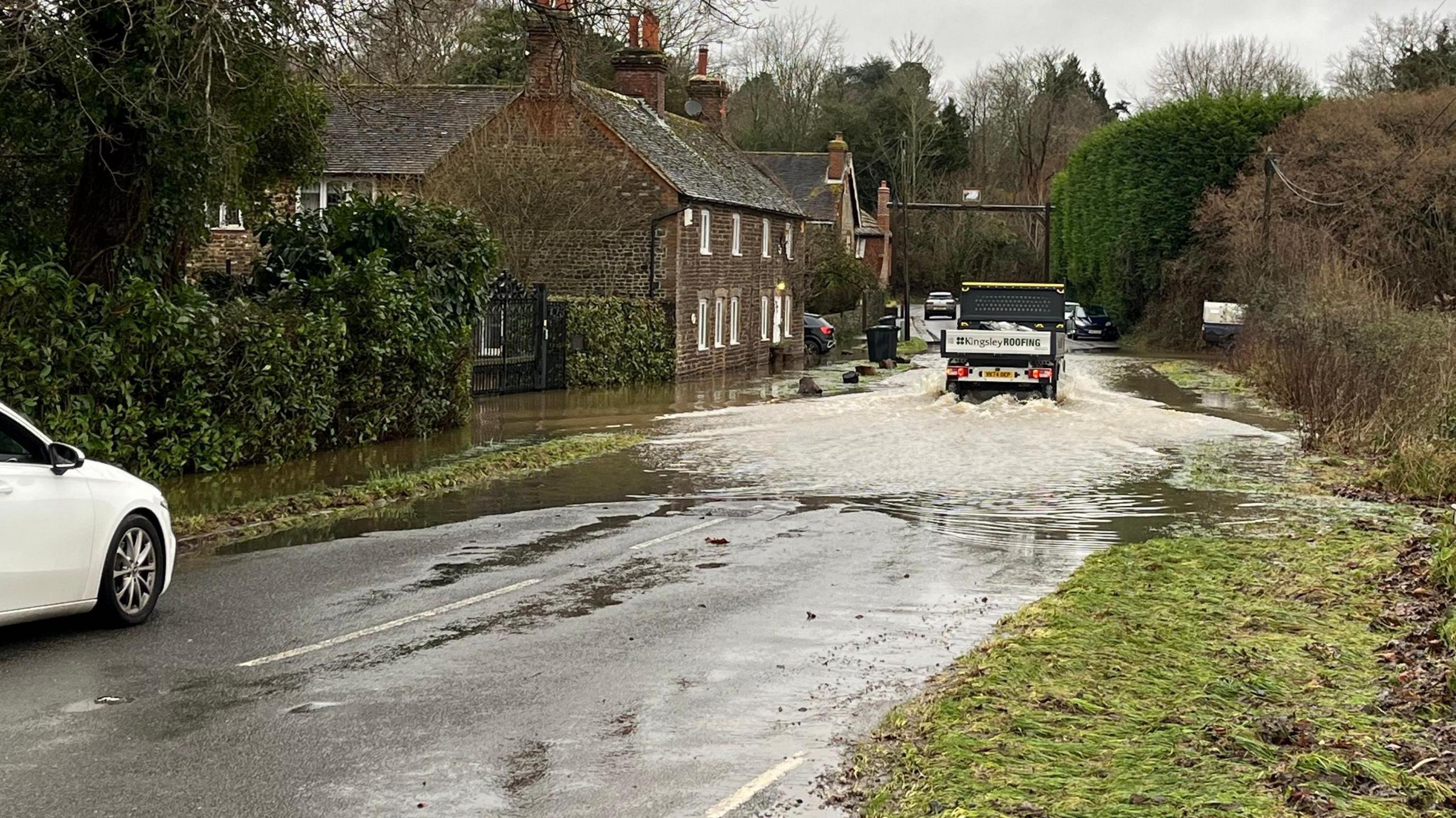 Flooding on the B2138 Lower Street Roadnear Fittleworth, West Sussex. A lorry can be seen driving through extensive rainfall on the road, which is flanked by houses to the left