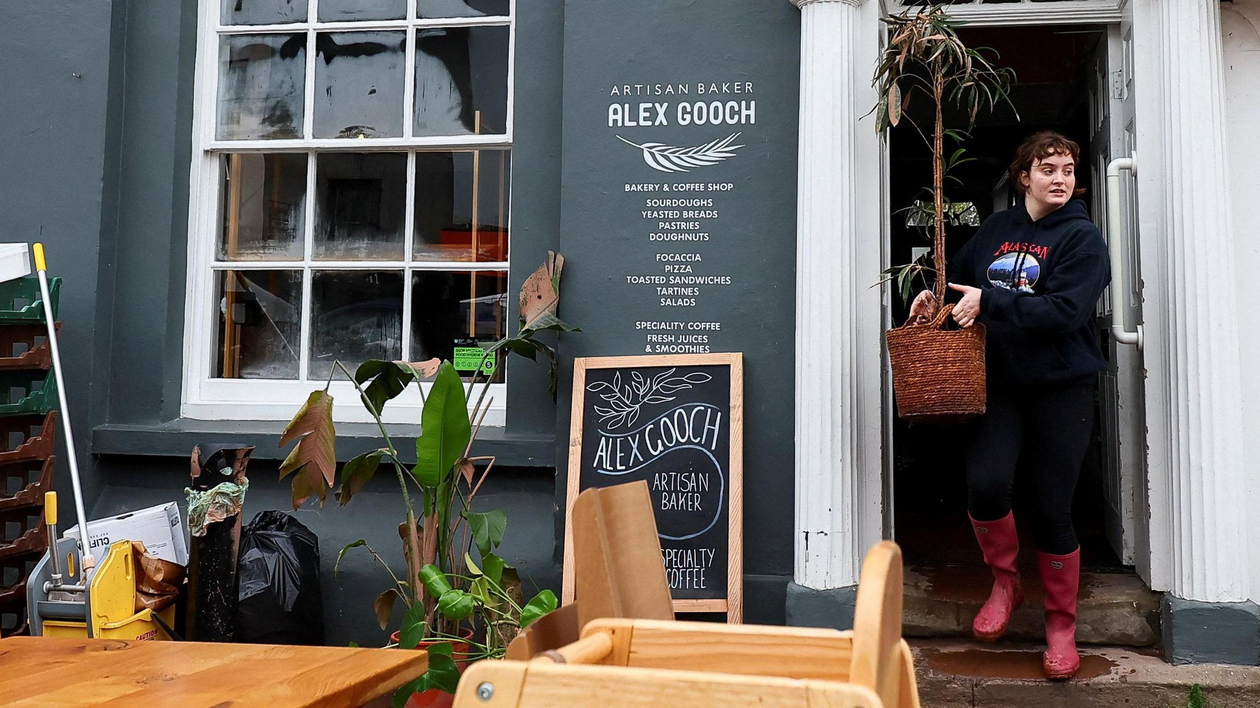 Woman carries items out of a bakery as items are piled up on the street