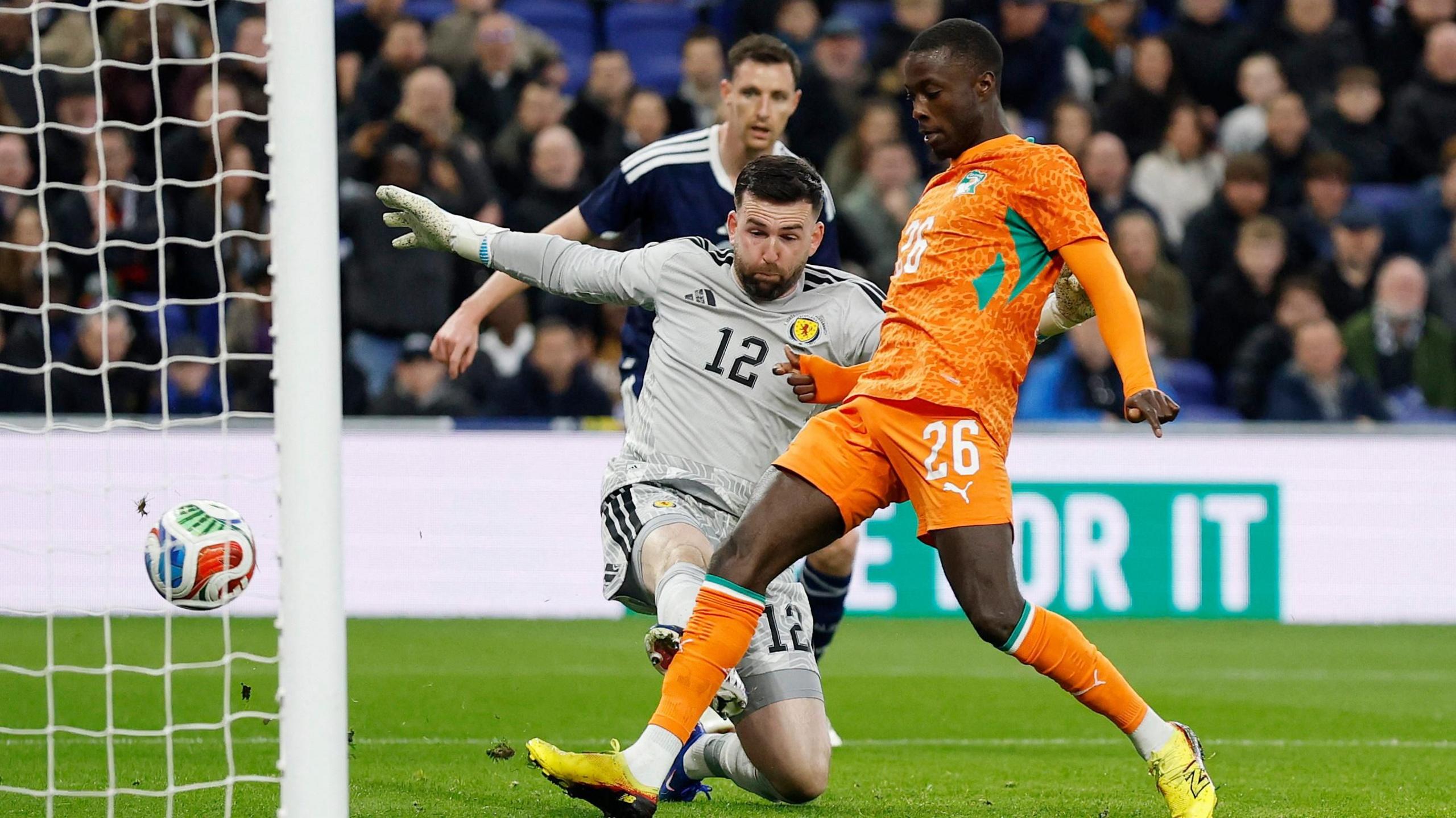 Ivory Coast's Nicolas Pepe wears an orange kit and scores their first goal past Scotland's Liam Kelly in grey.