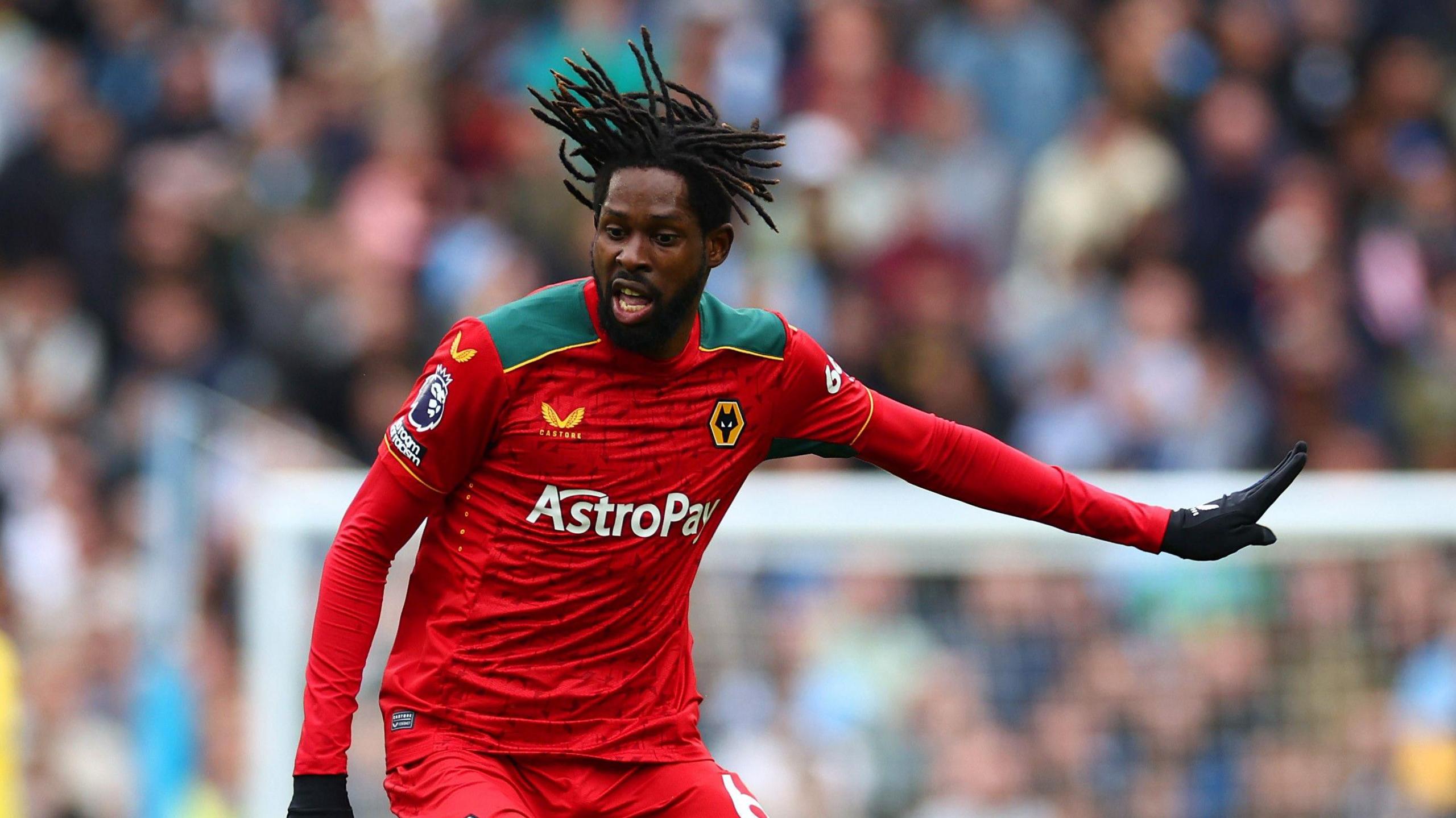 Boubacar Traore, wearing Wolves' all red away kit, pushes his left arm out to his side and looks at the ball (out of the picture). His right arm is down at his hip while his black dreadlocks are rising above his head, indicating he is running. 