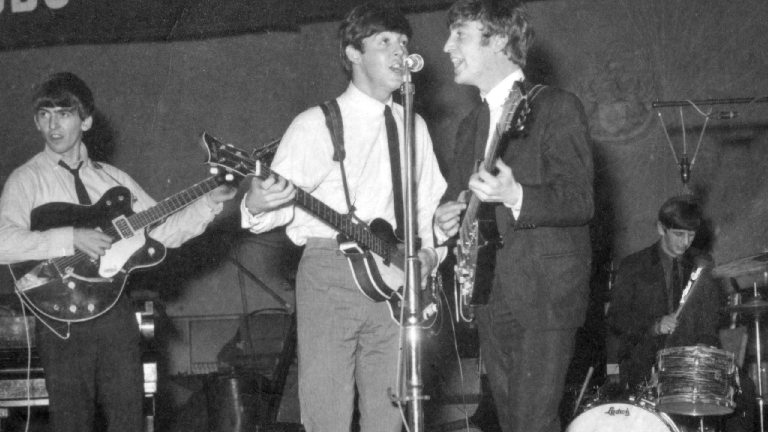 The Beatles playing on BBC radio with Paul McCartney and  George Harrison in shirts and a black rie while John Lennon and Ringo Starr are in full suit and tie