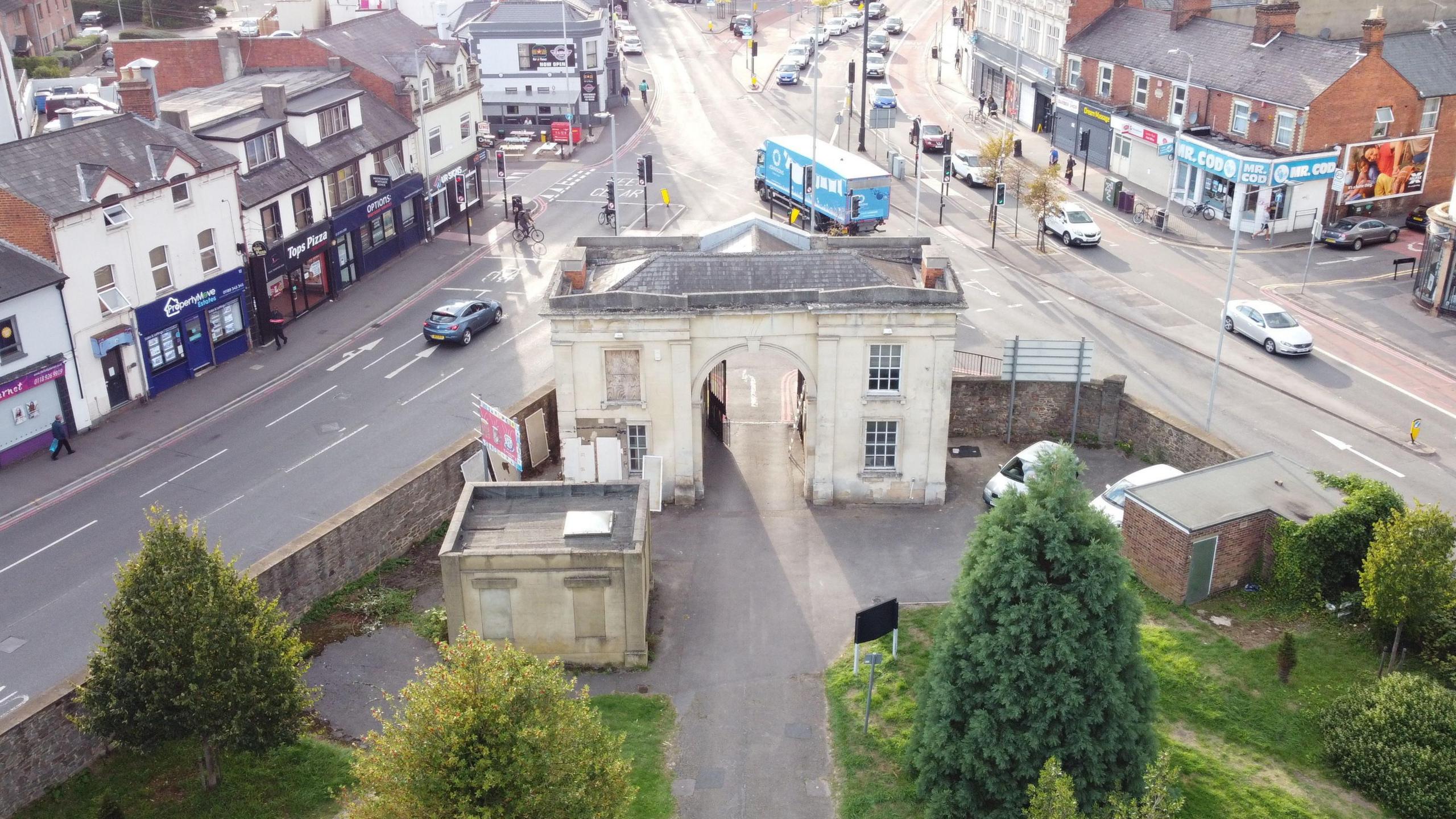 Drone view of the arch - a two-storey building with four windows (one blocked up). Two roads run either side of the building. Grass and trees within the cemetery grounds can be seen in the foreground