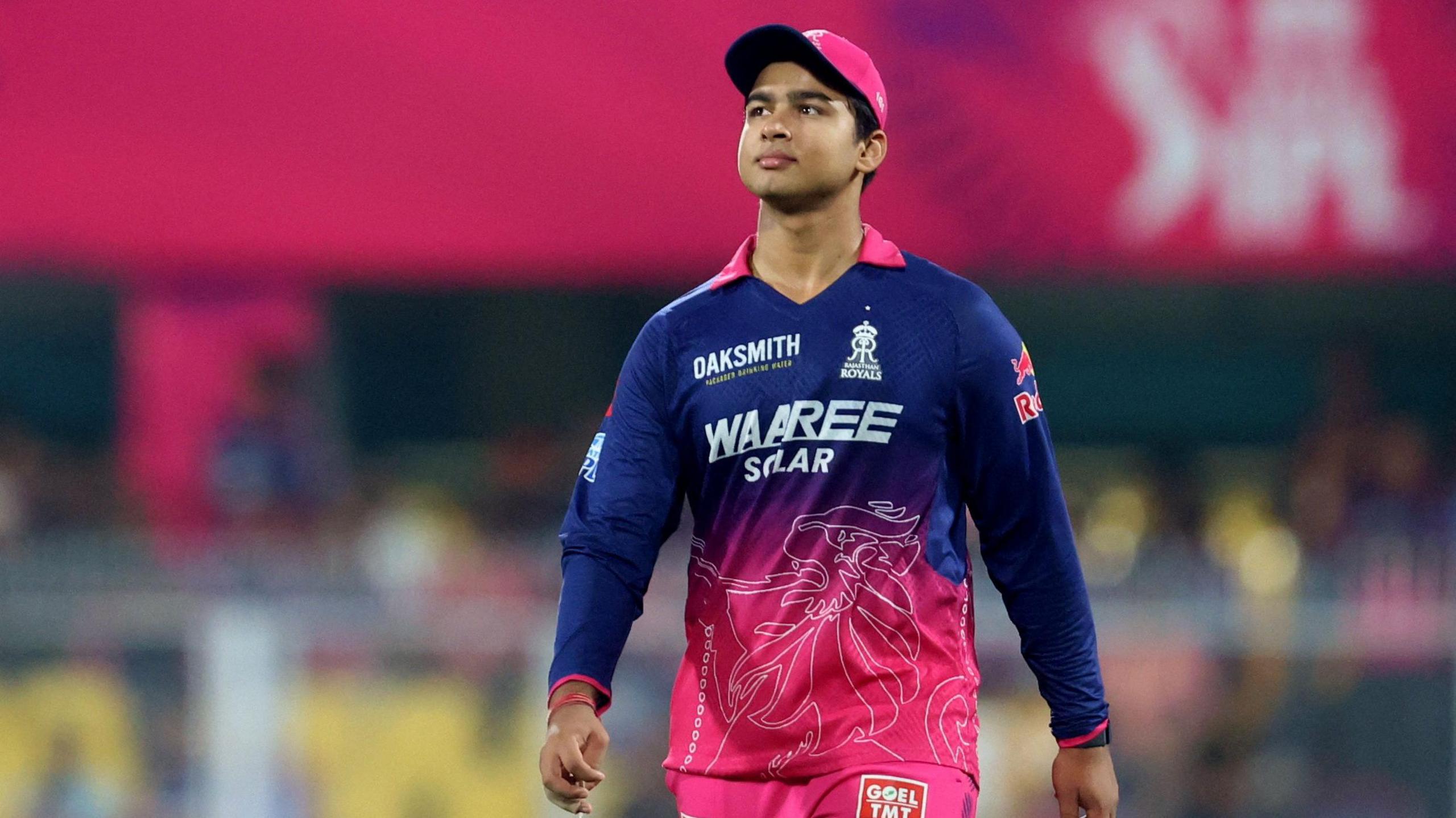 Vaibhav Suryavanshi wears a pink cap and a blue and pink shirt. He was walking on the field and looking into the distance