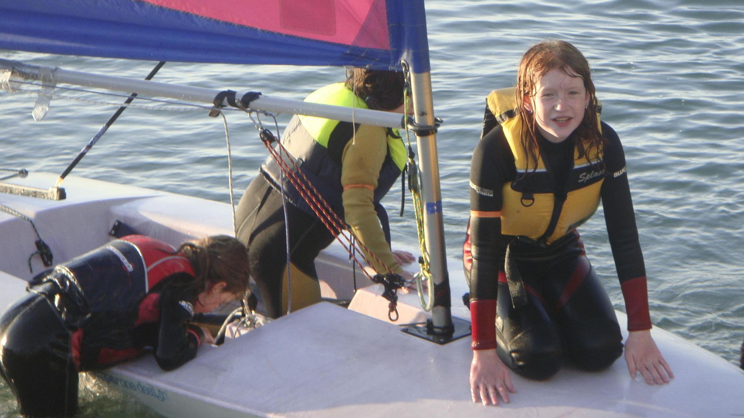 Three children are on a small dinghy with one kneeling on the bow looking at the camera