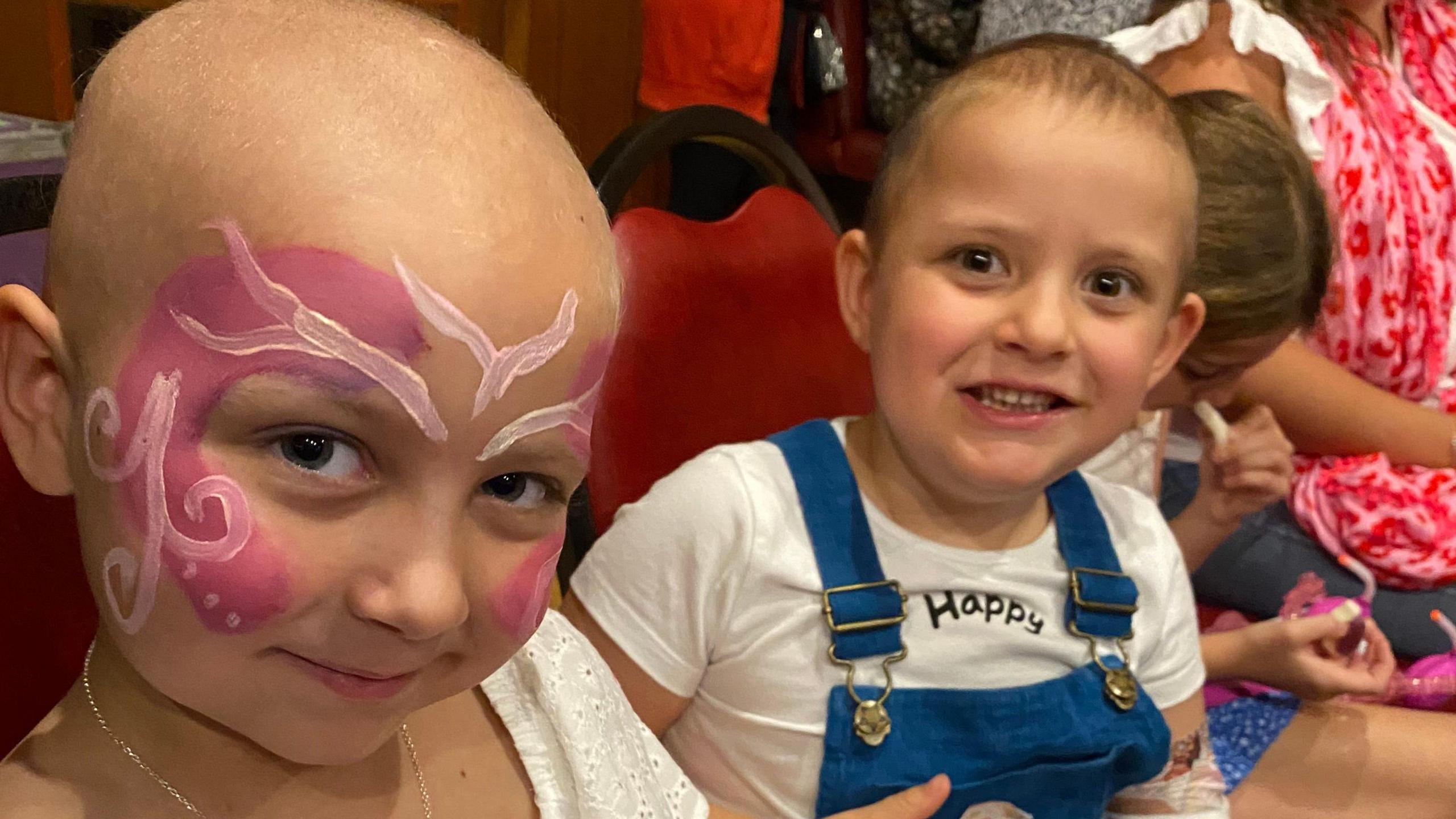 Betsy (left) and Lacie. Both have lost their hair and Betsy is wearing pink and white swirly face paint.  