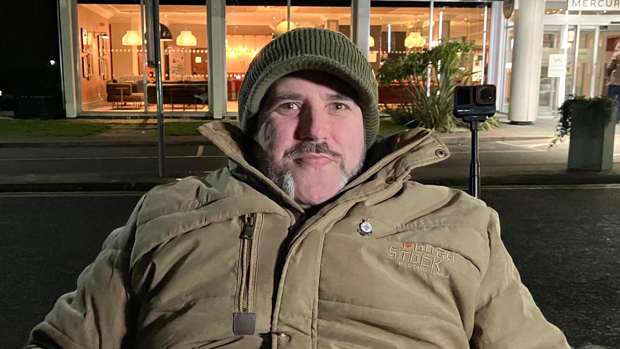 Nick Wilson who took part in the Big Sleep Out is seen in the picture, wearing a light olive-coloured coat and dark green hat. 