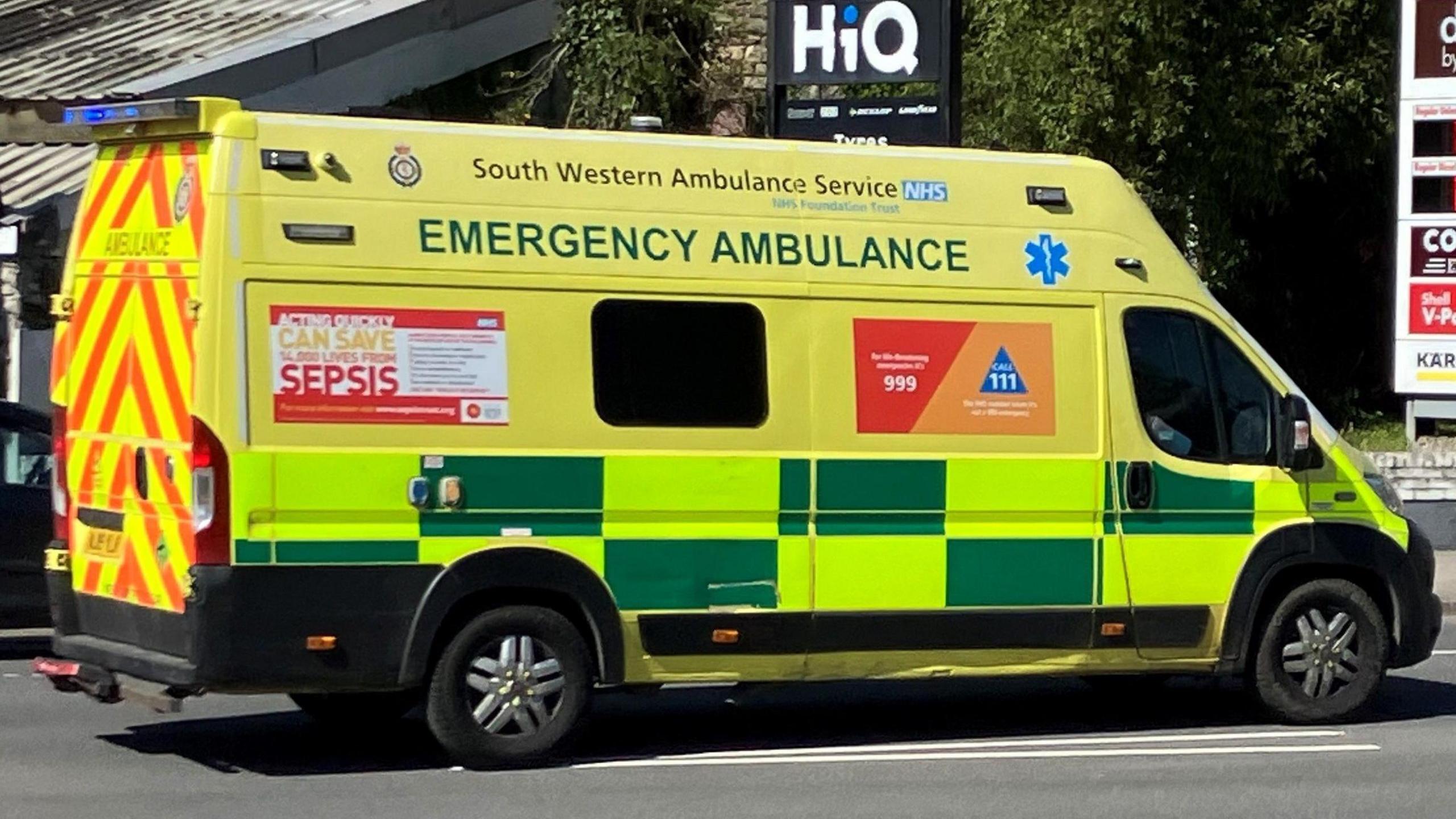 An ambulance speeding past a petrol station with blue flashing lights.